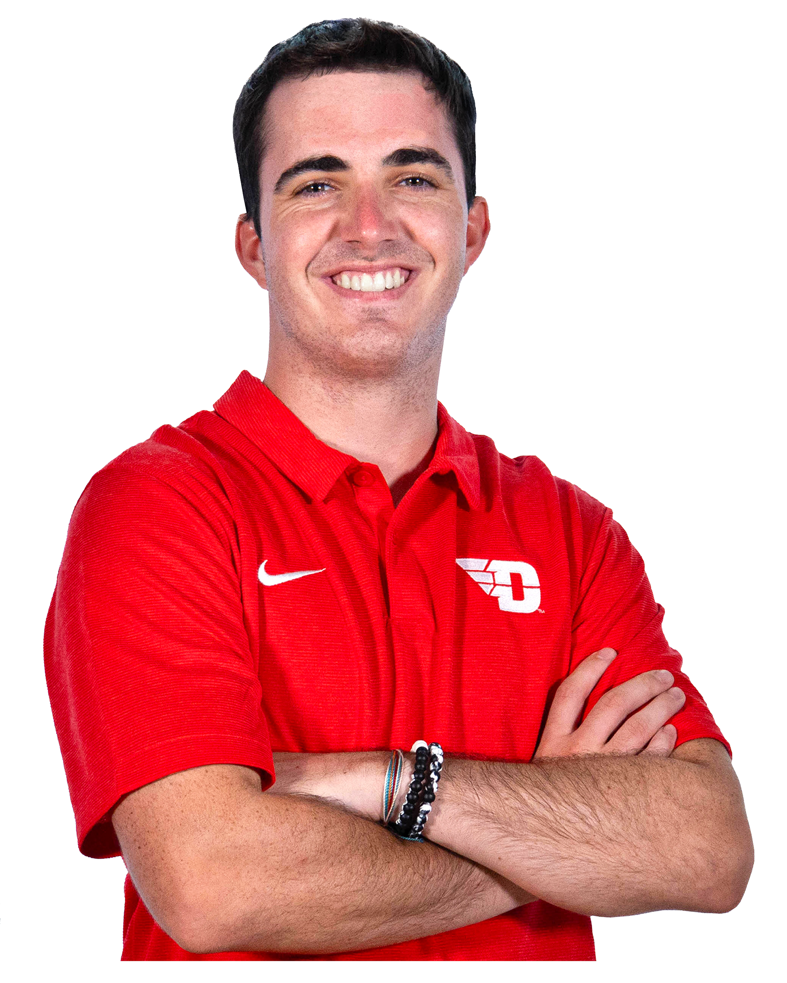 A young man with dark hair, wearing a red polo shirt with a logo and white Nike swoosh, smiling and crossing his arms, adorned with multiple bracelets.