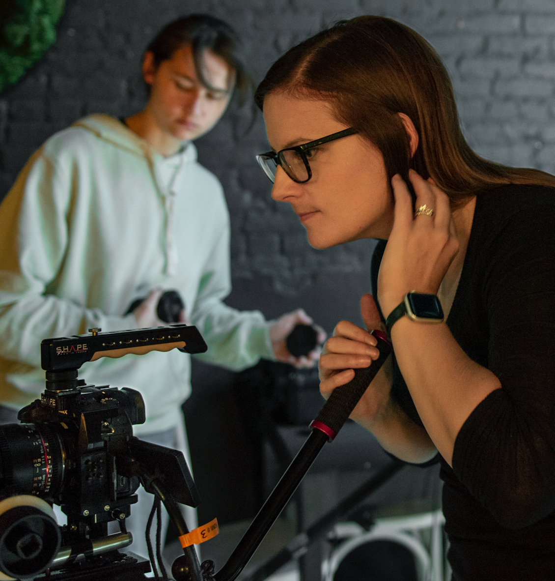 Two women working on 3D camera setup in a room with a black brick wall.