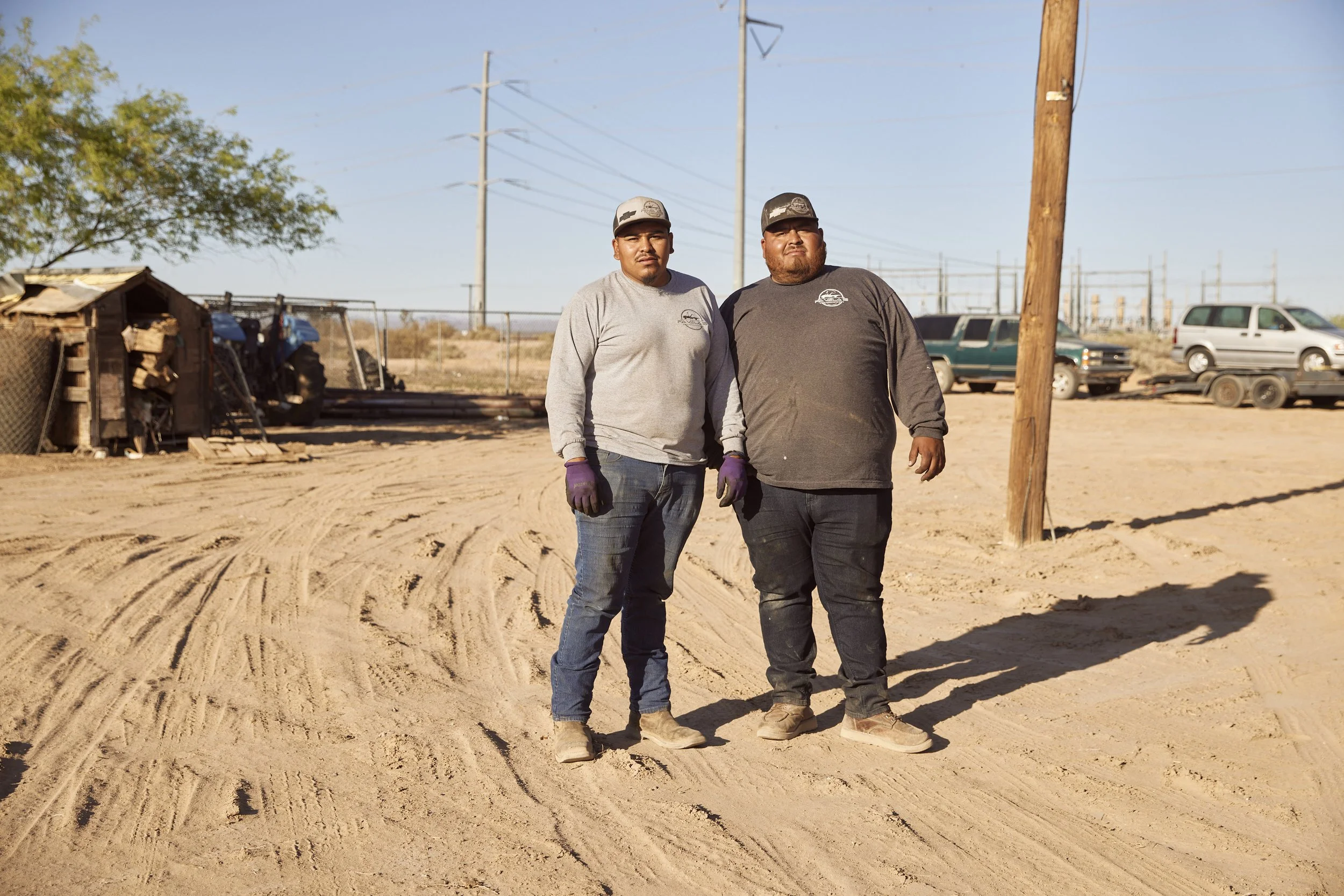 Portrait of two men in work clothes standing near trucks and sheds in Randolph, Arizona — documentary photo by Matt Martian, editorial photographer in Phoenix, Arizona