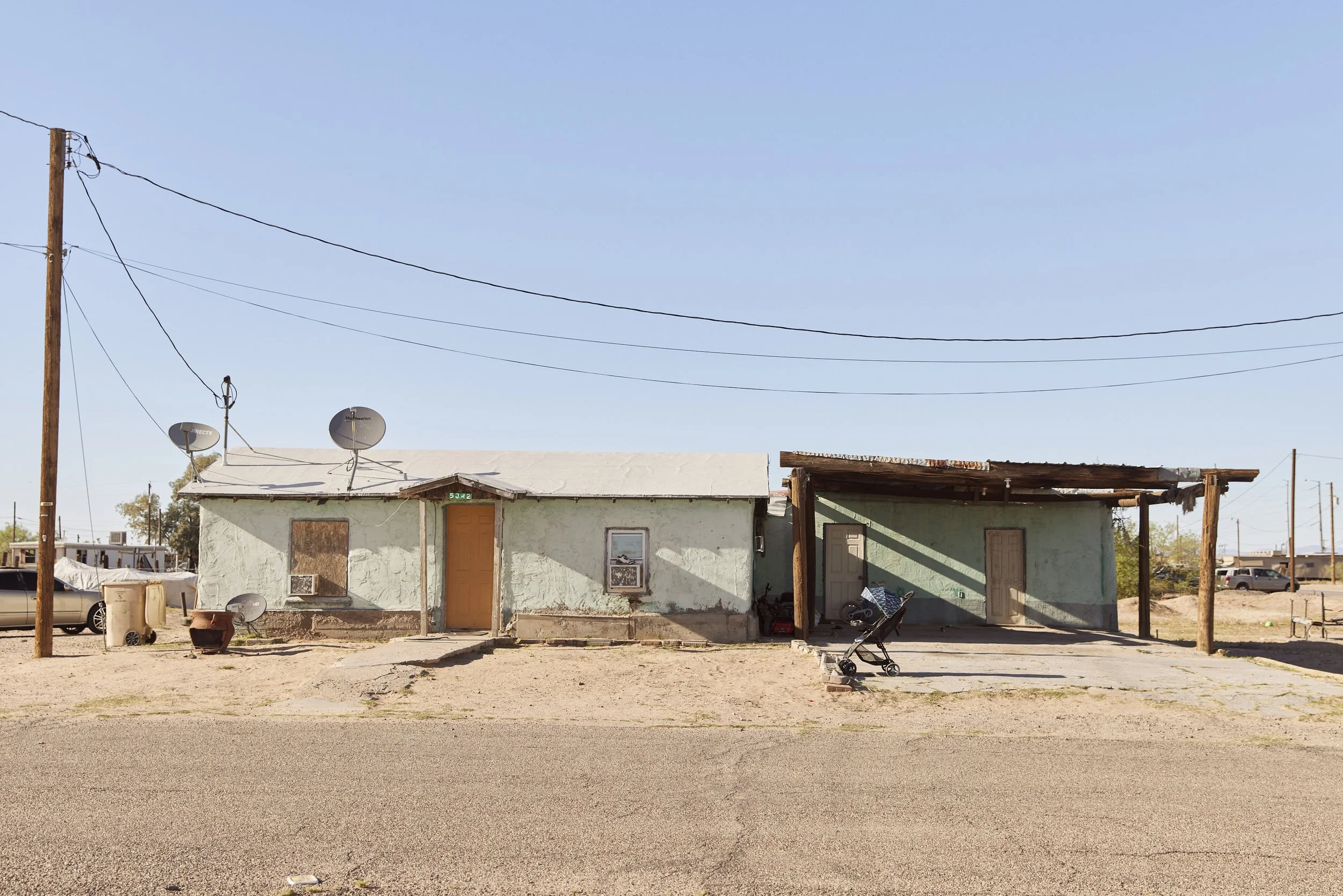 Small green house with satellite dishes in a dusty residential area of Randolph, Arizona — photographed by Matt Martian, editorial photographer in Phoenix, Arizona