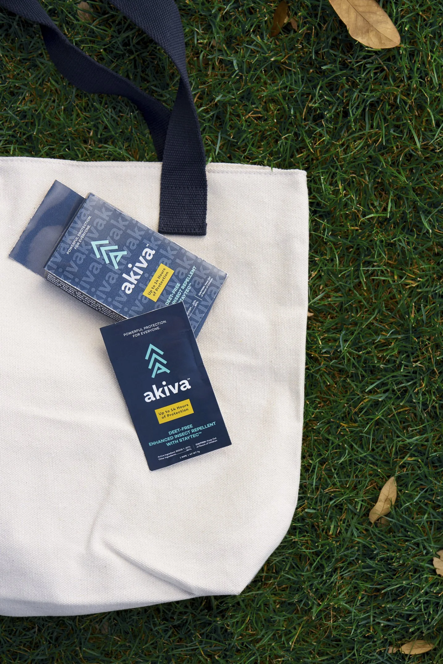 Akiva insect repellent packet and box on a canvas tote bag on grass