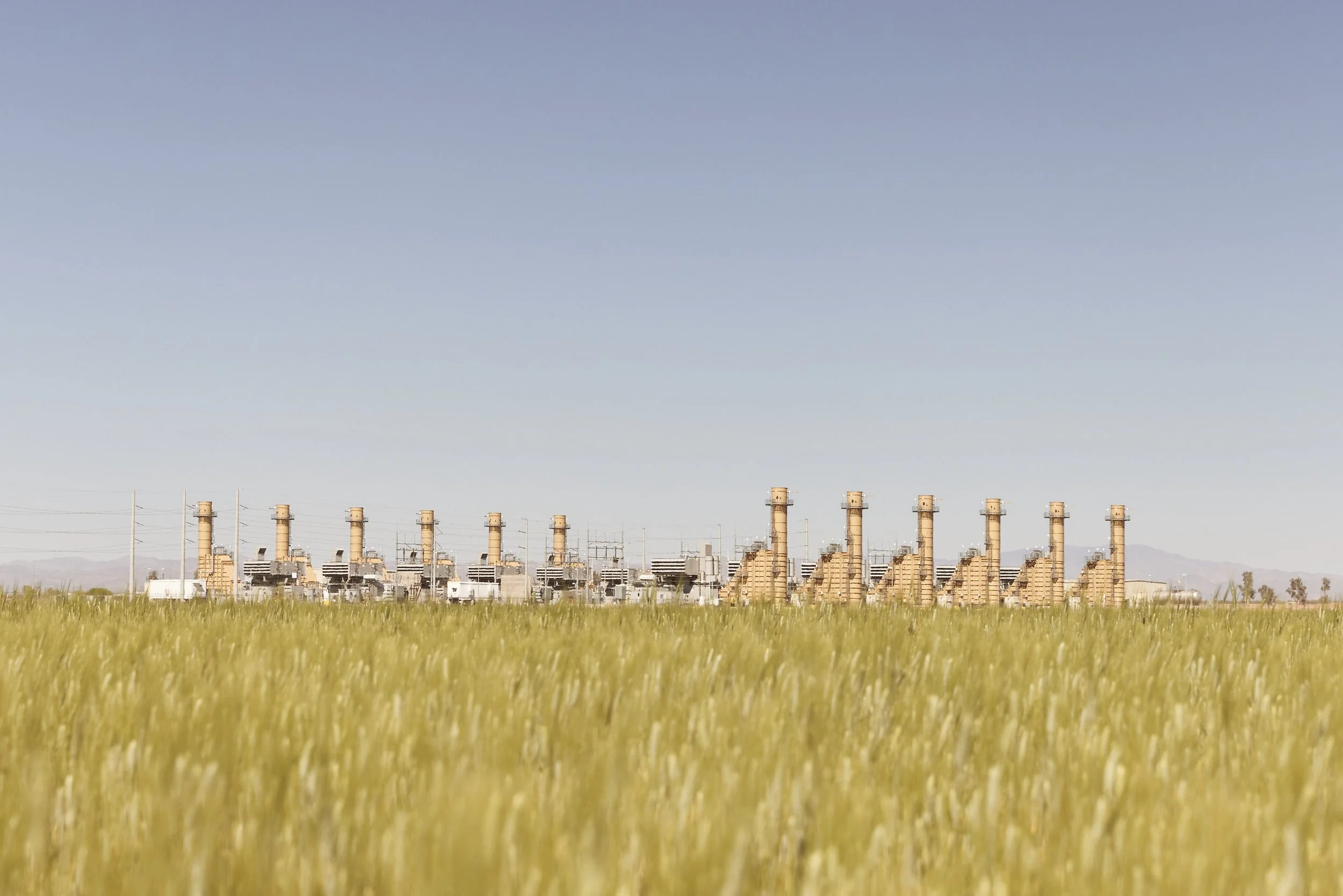 Distant view of smokestacks beyond a green field near an industrial site in Randolph, Arizona — photographed by Matt Martian, editorial photographer based in Phoenix, Arizona