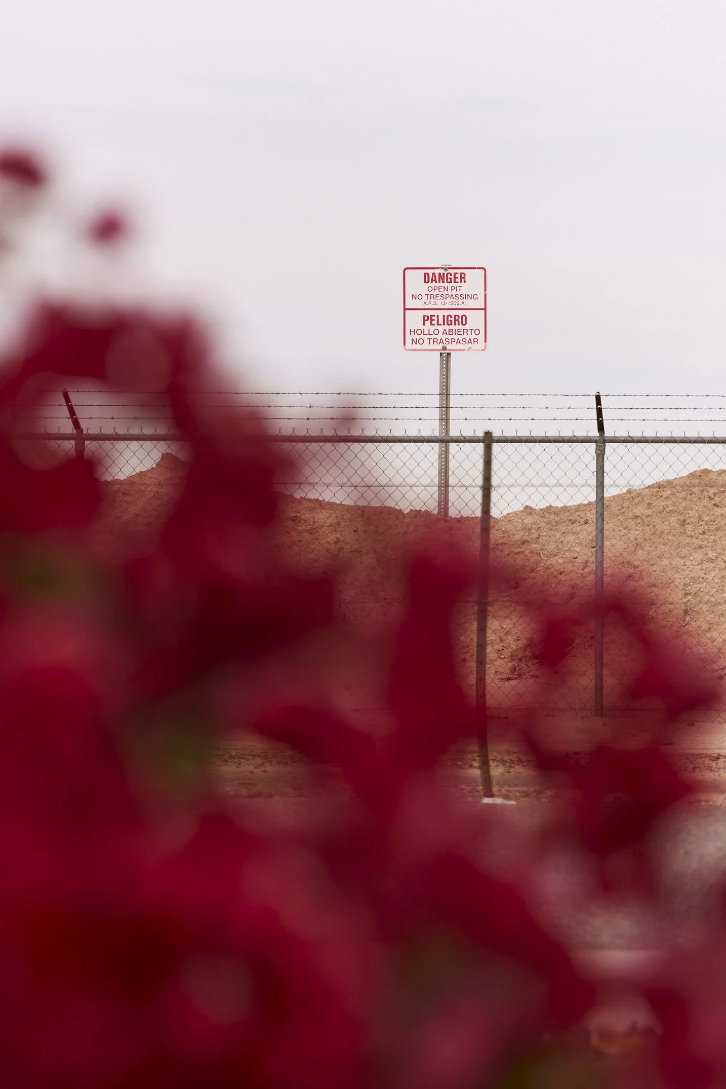 A "Danger" sign warning of no trespassing on a dirt mound under a cloudy sky. Captured by Phoenix-based editorial photographer Matt Martian