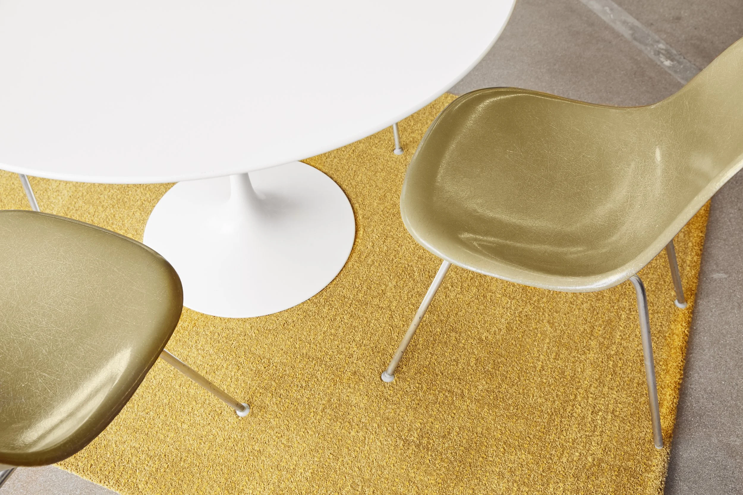 Two beige Eames molded plastic chairs with metal legs next to a white pedestal table on a yellow carpet.