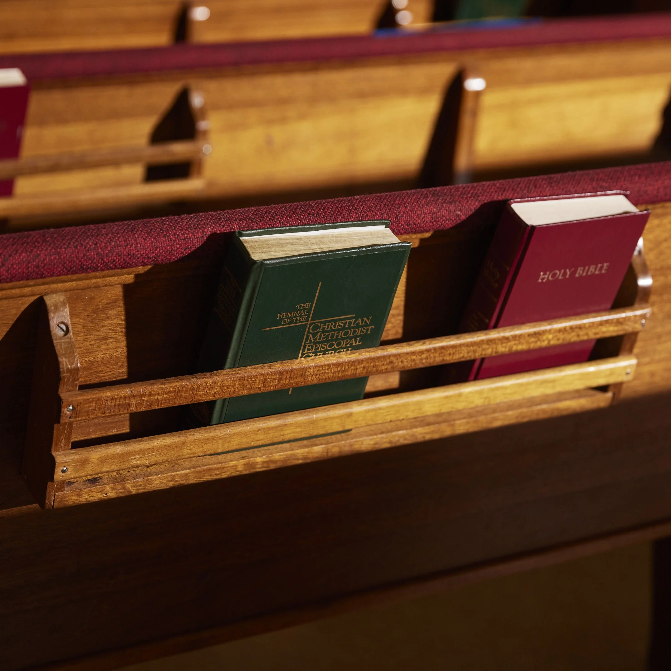 Church pew with hymnals and a Bible in a wooden rack.