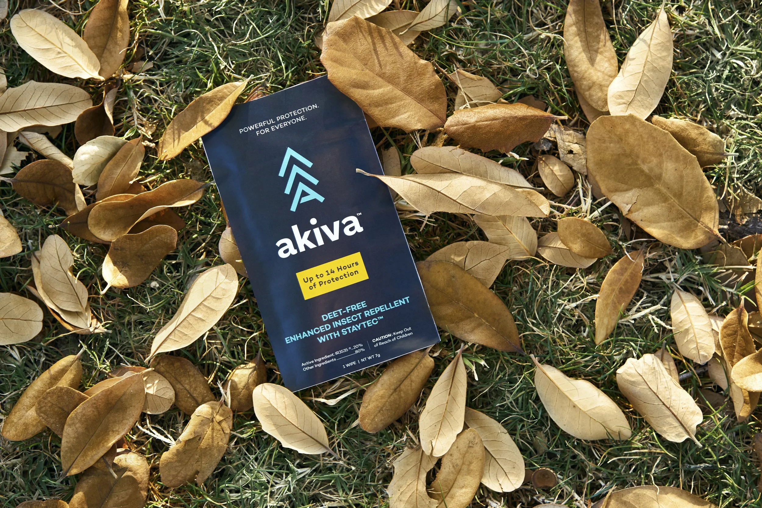 Insect repellent packet labeled 'akiva' on grass with dry leaves.