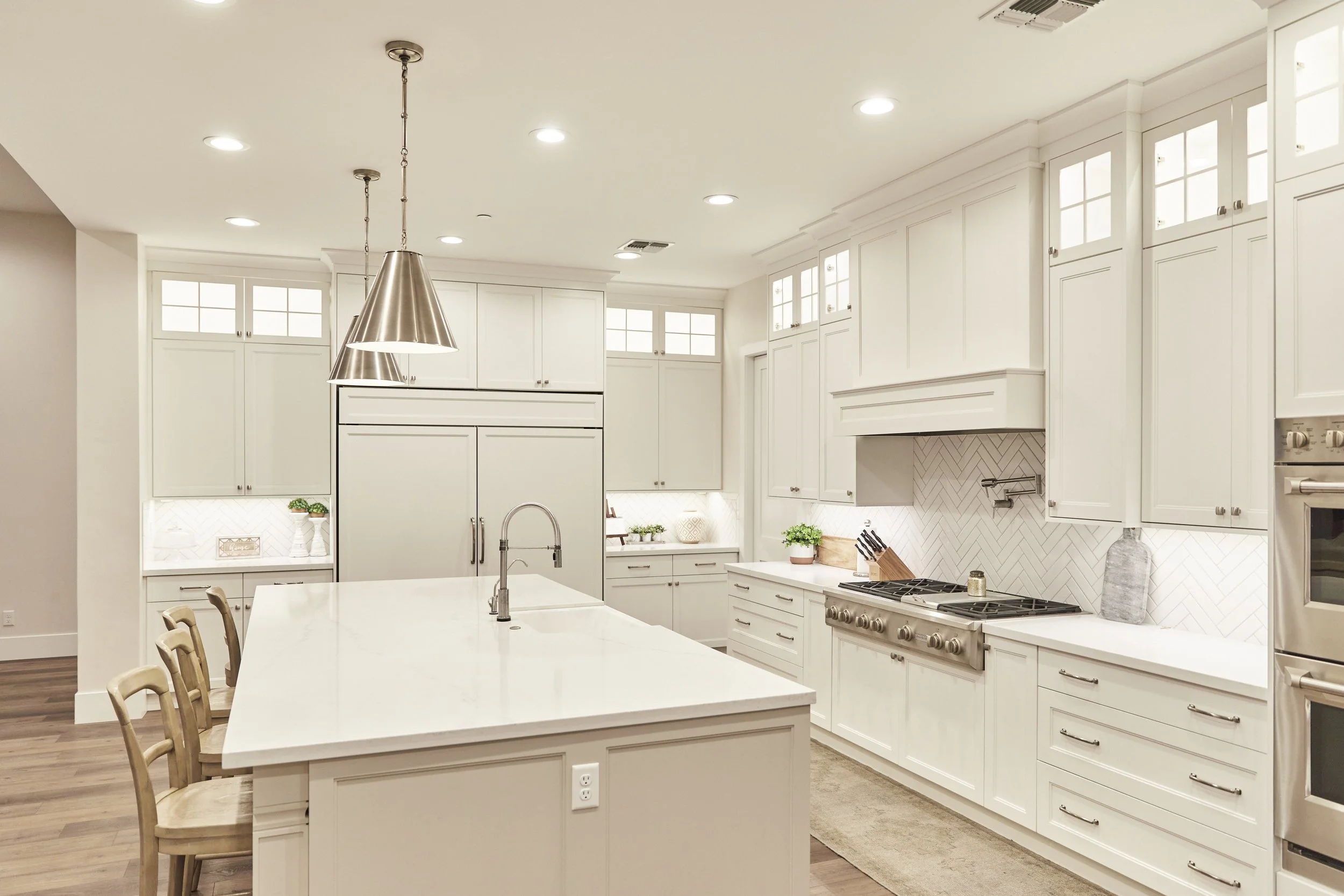Modern white kitchen with island, pendant lights, stainless steel appliances, and herringbone backsplash.