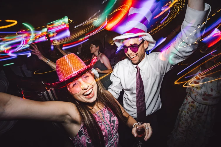 People celebrating at a party wearing colorful hats and glasses with vibrant light trails in the background