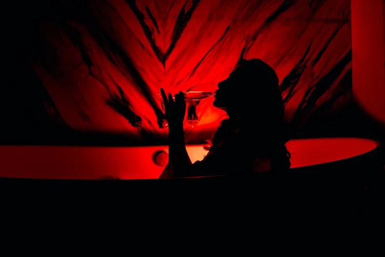 Silhouette of a woman drinking from a glass against a red abstract background.