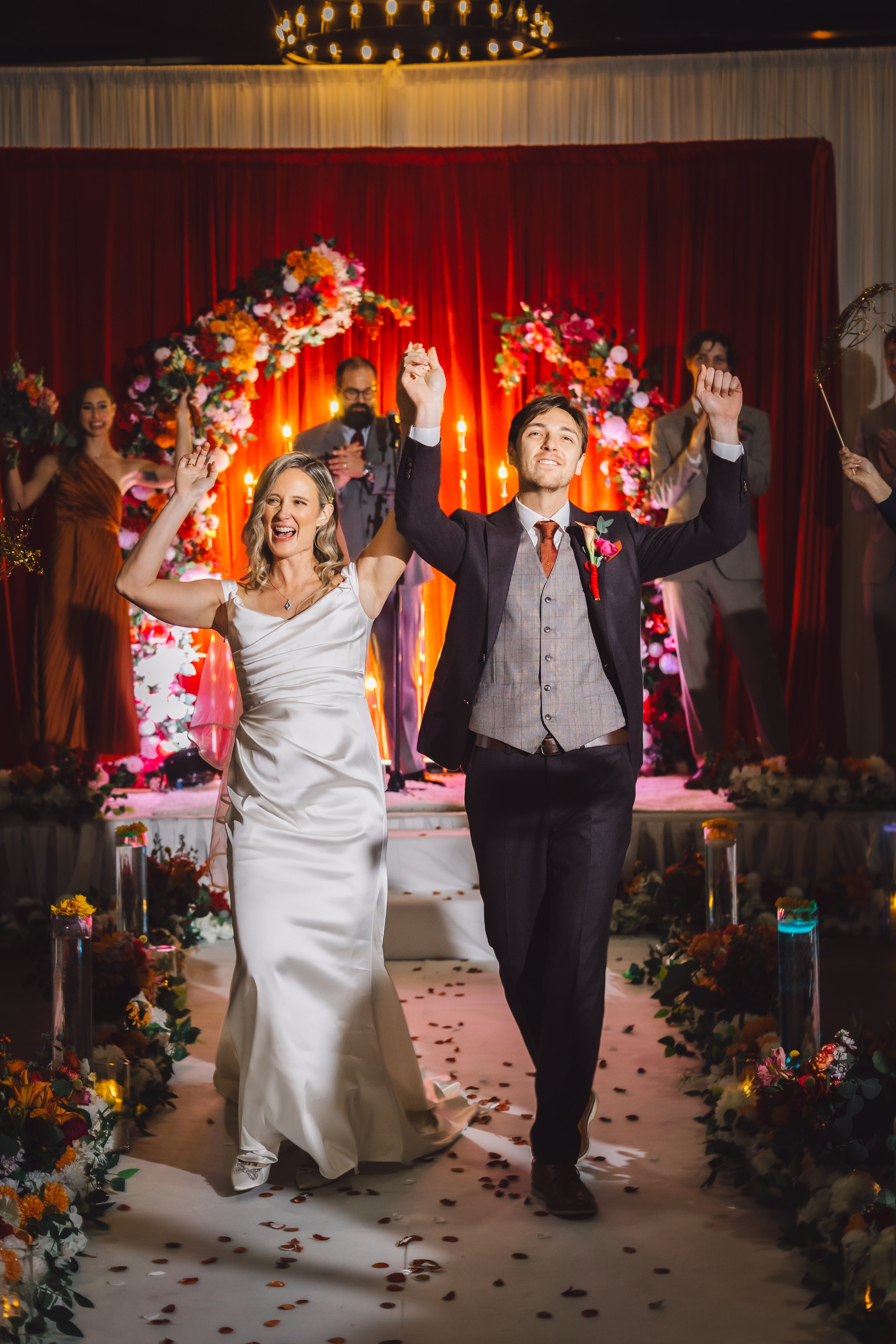 Bride and groom walking down the aisle while celebrating their wedding ceremony, with guests and wedding staff applauding in the background.