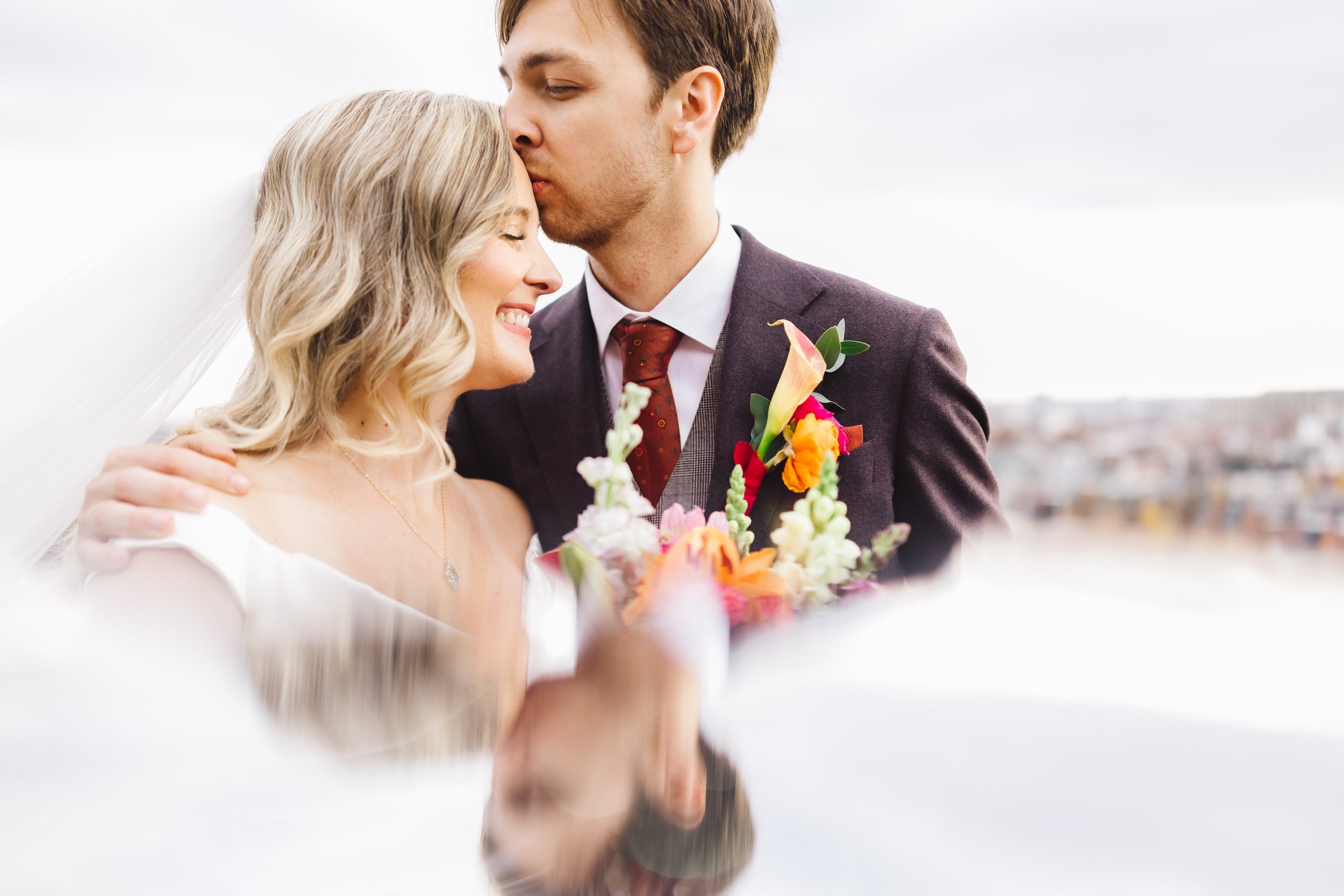 A bride and groom sharing a romantic moment, with the groom kissing the bride on the forehead, during their wedding.