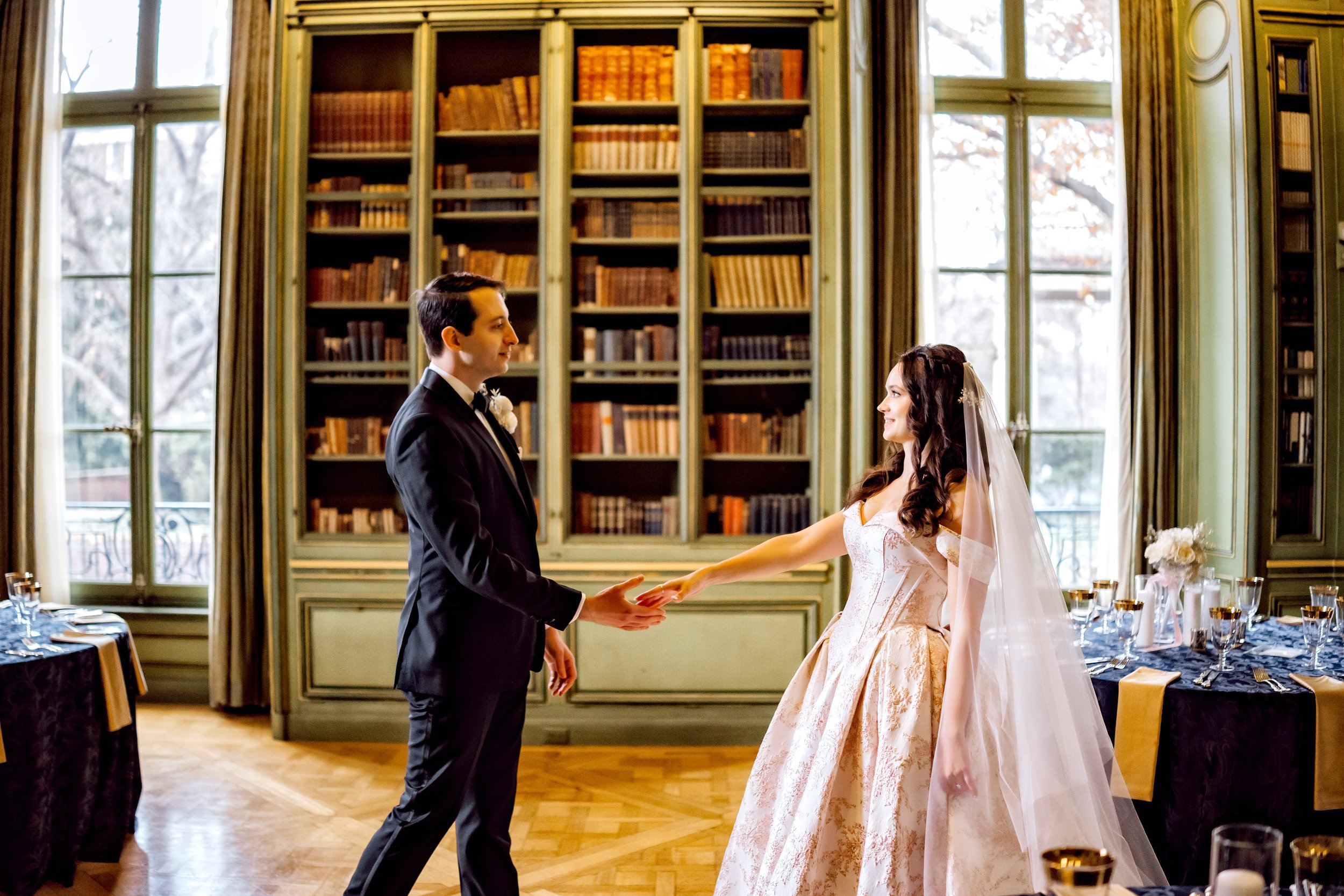 A bride and groom holding hands in a library during their wedding reception.