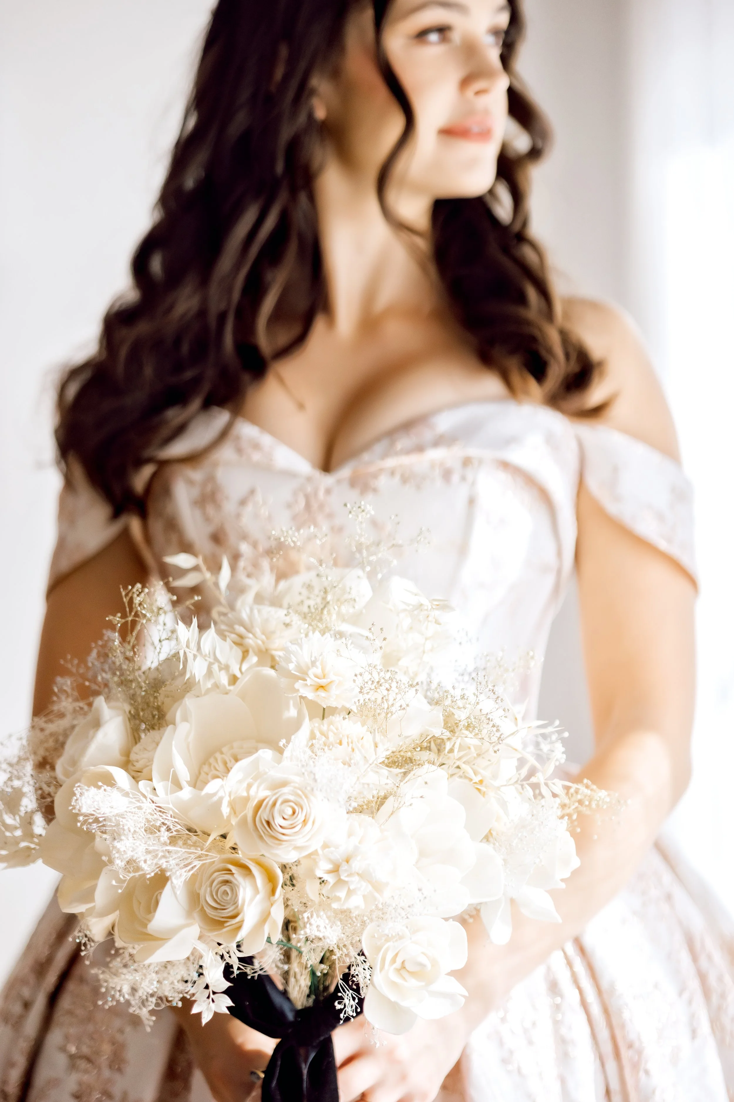 A bride in an off-the-shoulder wedding dress holding a bouquet of white flowers.