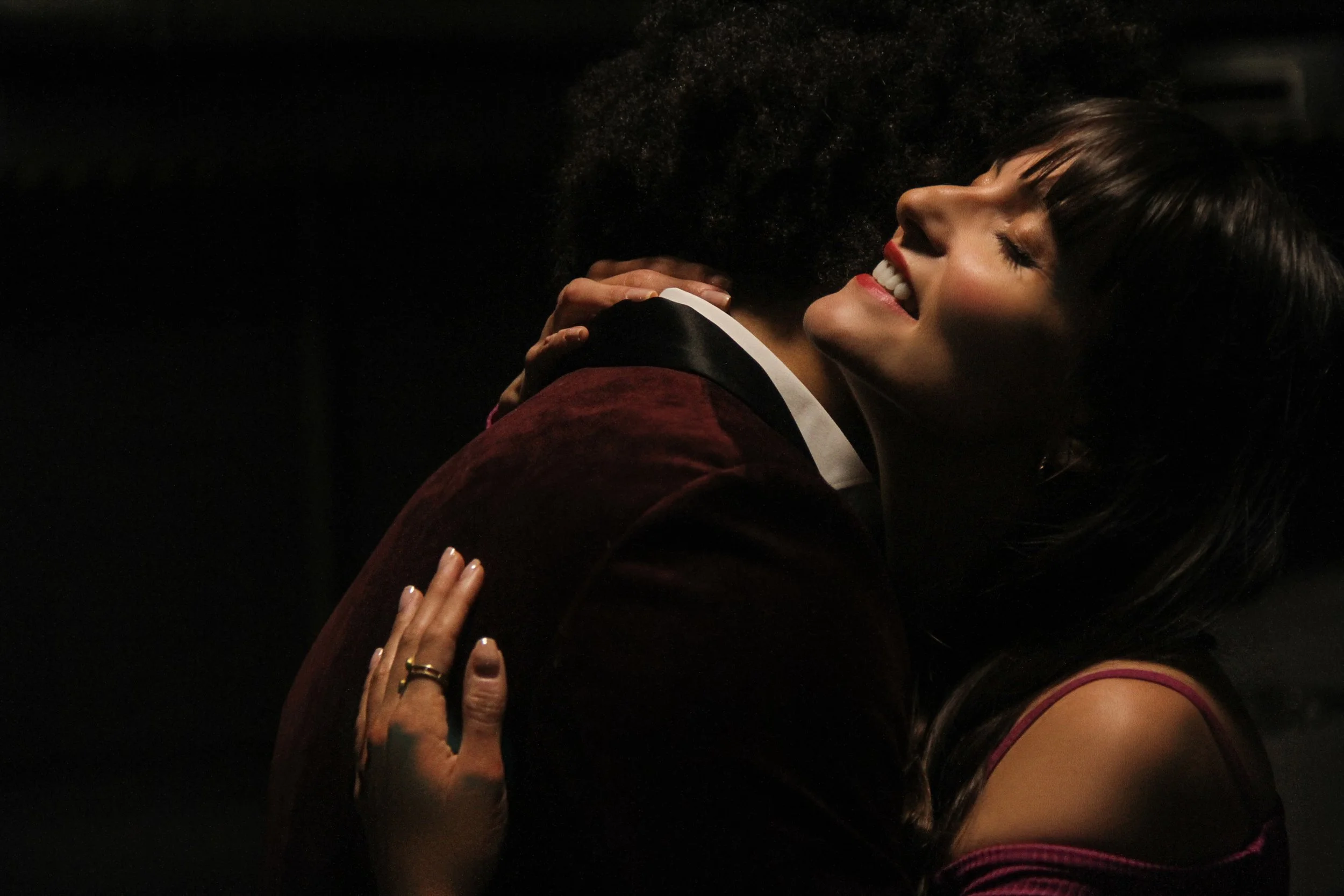 Two women hugging and smiling with their eyes closed, one with dark hair and the other with curly hair, in a close, intimate embrace.