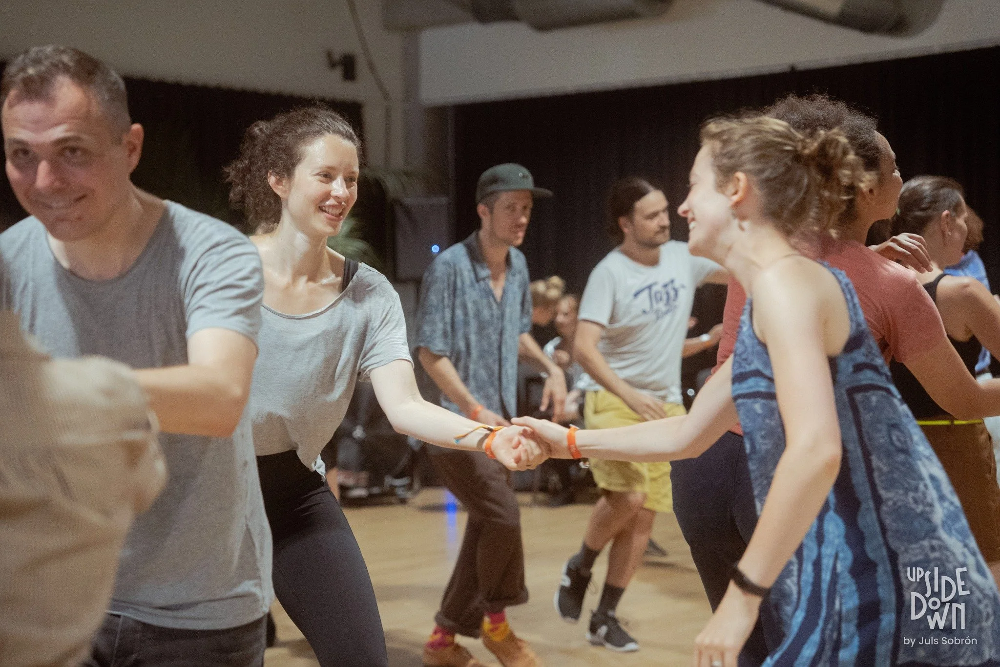 People dancing and holding hands in a lively social dance event, smiling and enjoying the music.
