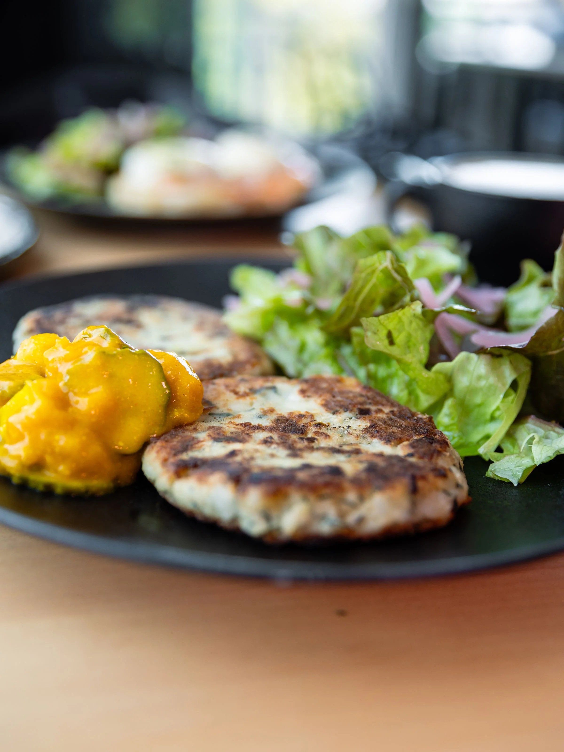 A close-up of a plate with grilled chicken, a salad with green and purple lettuce, and a baked potato topped with melted cheese and sour cream on a wooden table.