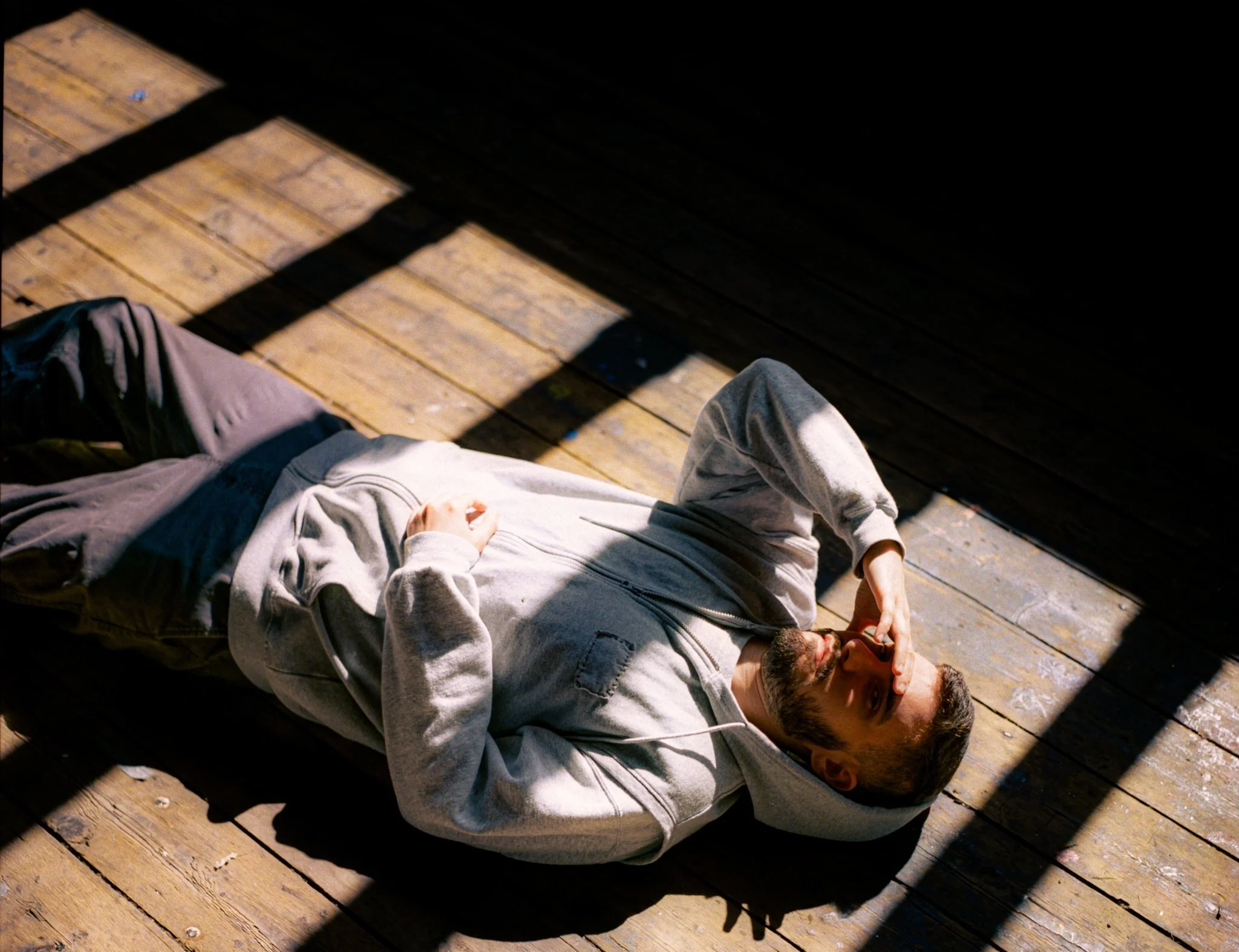Individual lying on a wooden floor, sunlight creating peaceful shadows.