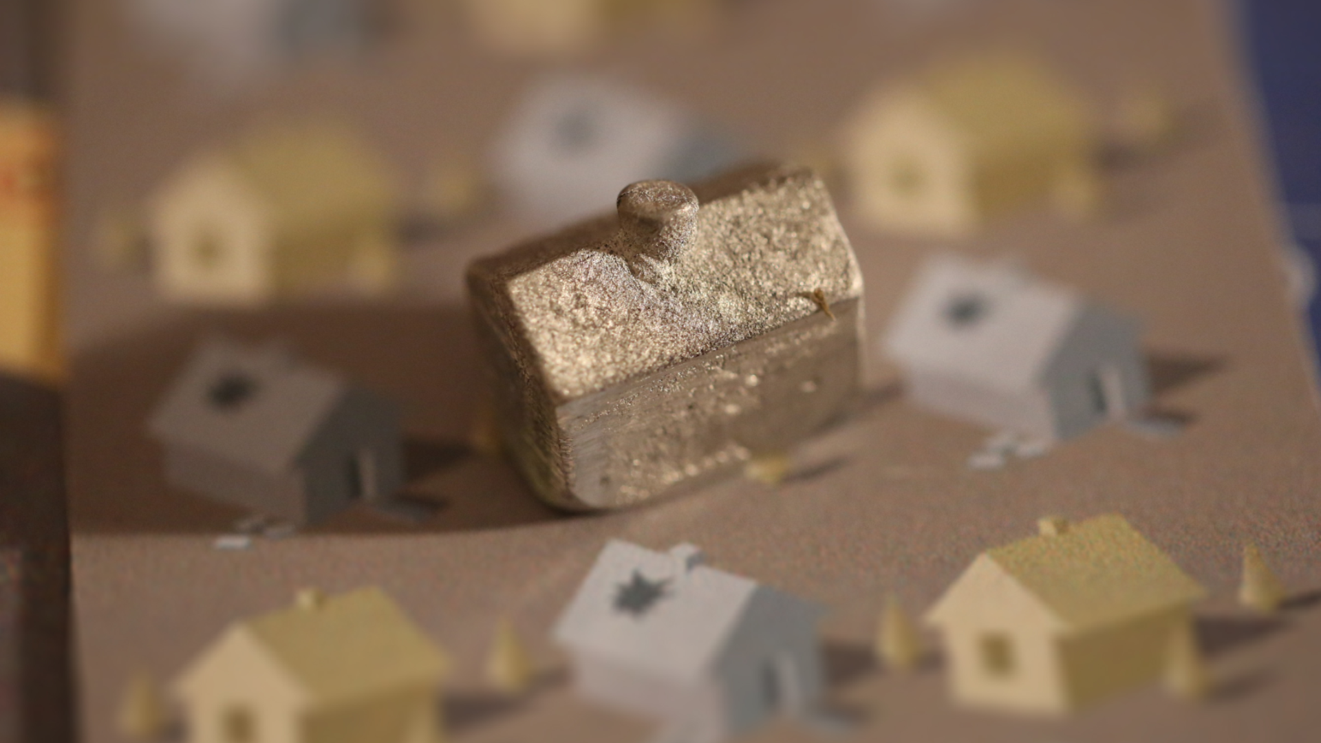 Close-up of a metallic game piece shaped like a house on a board with other game pieces and decorated pieces resembling houses.