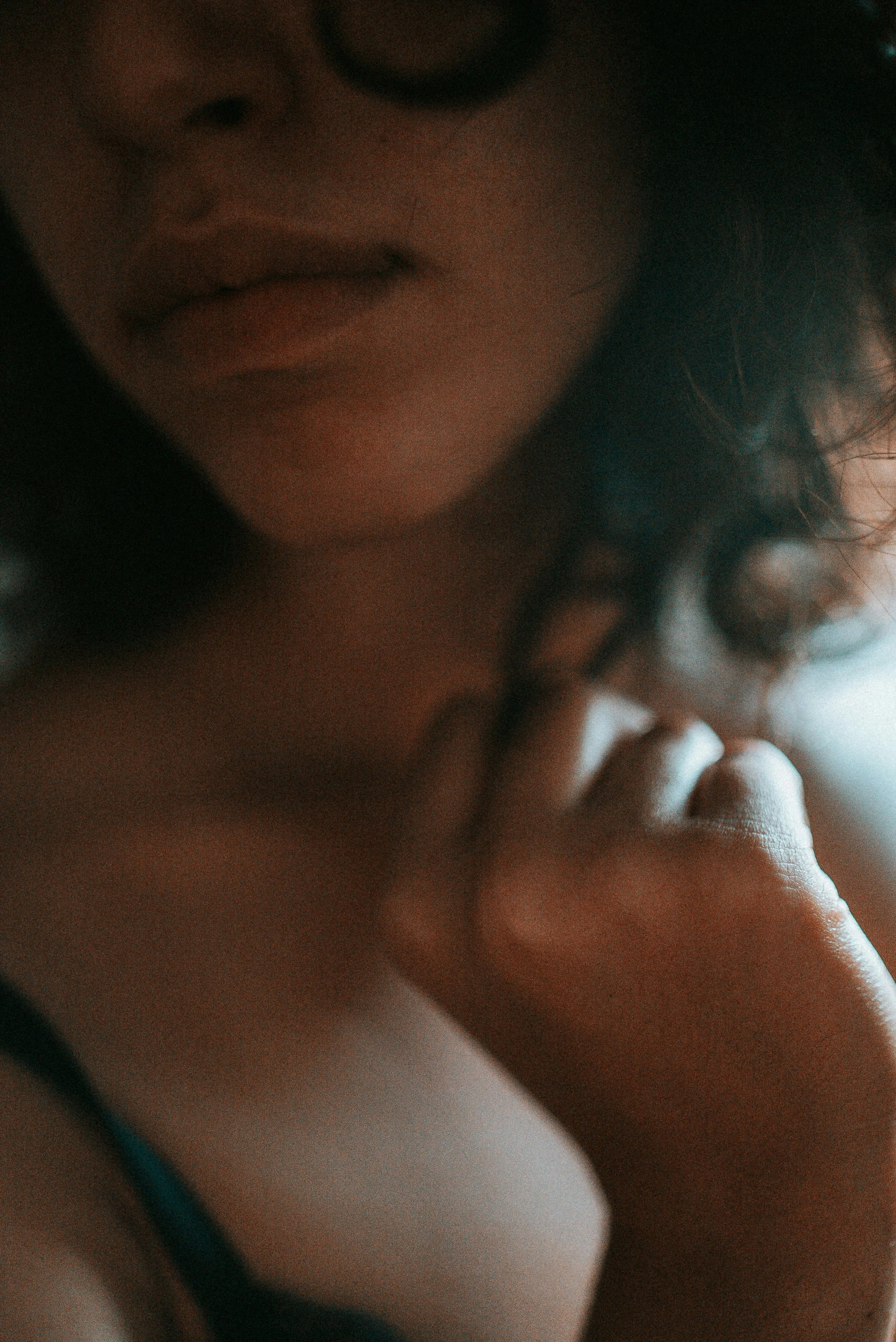 Portrait en gros plan d'une femme avec un visage partiellement visible, portant des lunettes, touchant son menton avec une main, sous une lumière douce.