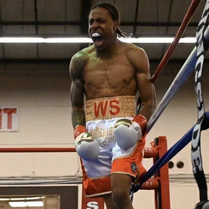 Boxer in the ring, shouting with gloves on, shirtless, wearing orange and white shorts.