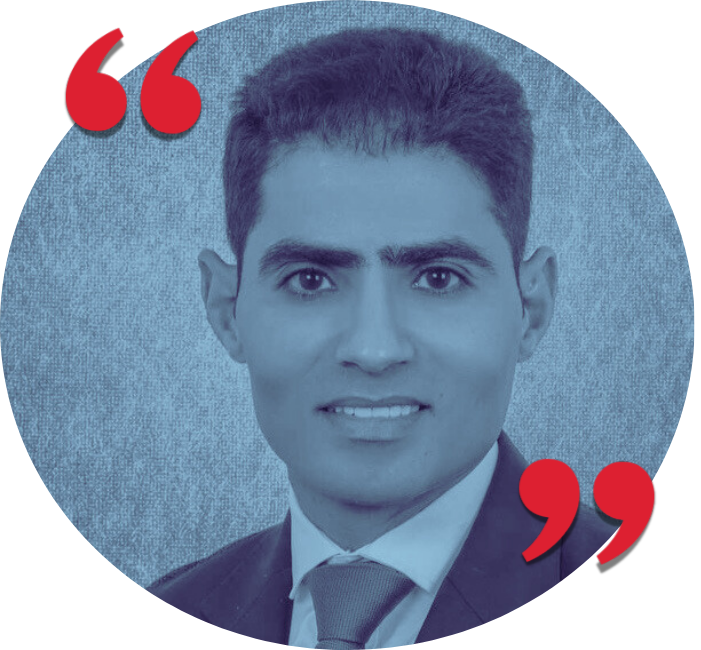 Black and white professional portrait of a young man in a suit and tie, smiling, with red quotation marks in the top left and bottom right corners.