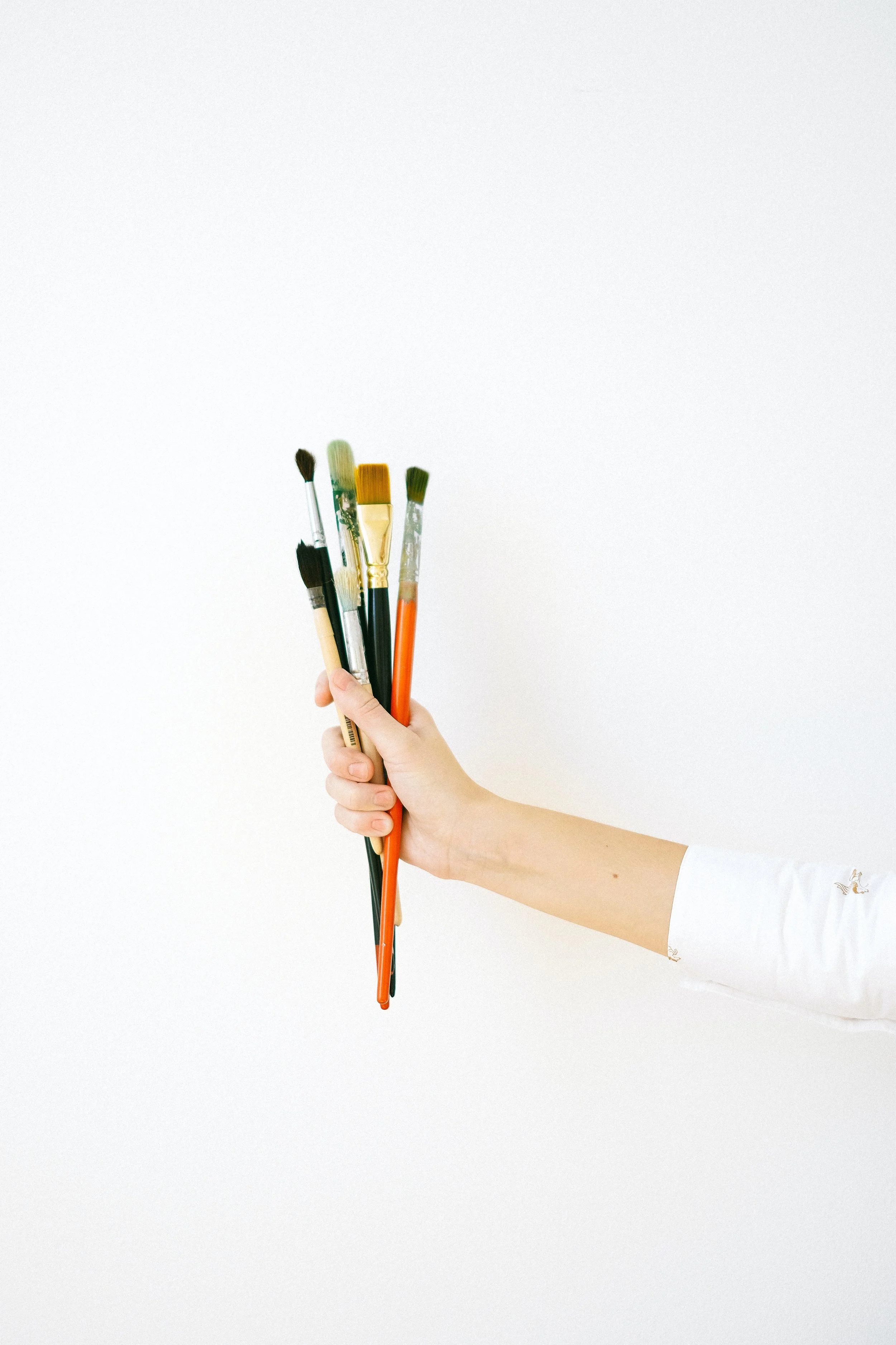 A hand holding several paintbrushes against a white background.