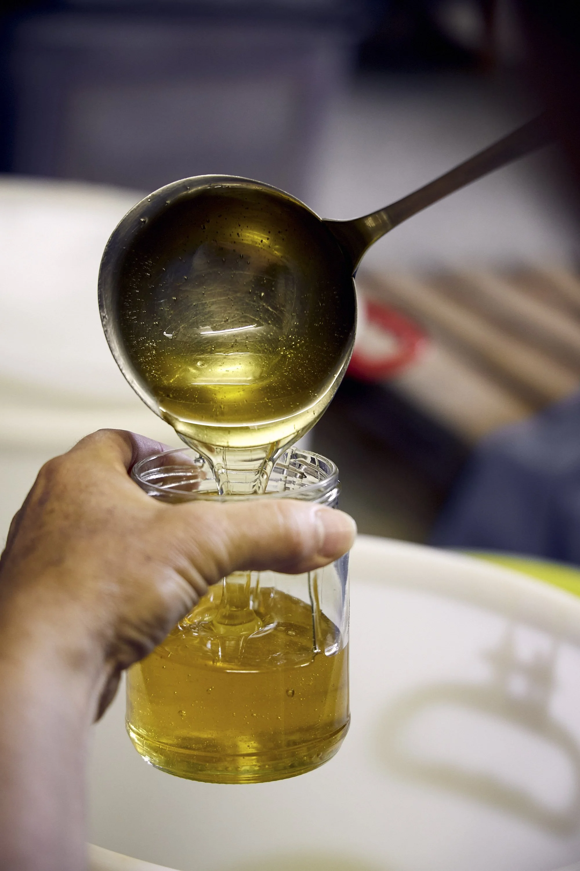 Frischer Honig wird mit einer Kelle in ein Glas gefüllt