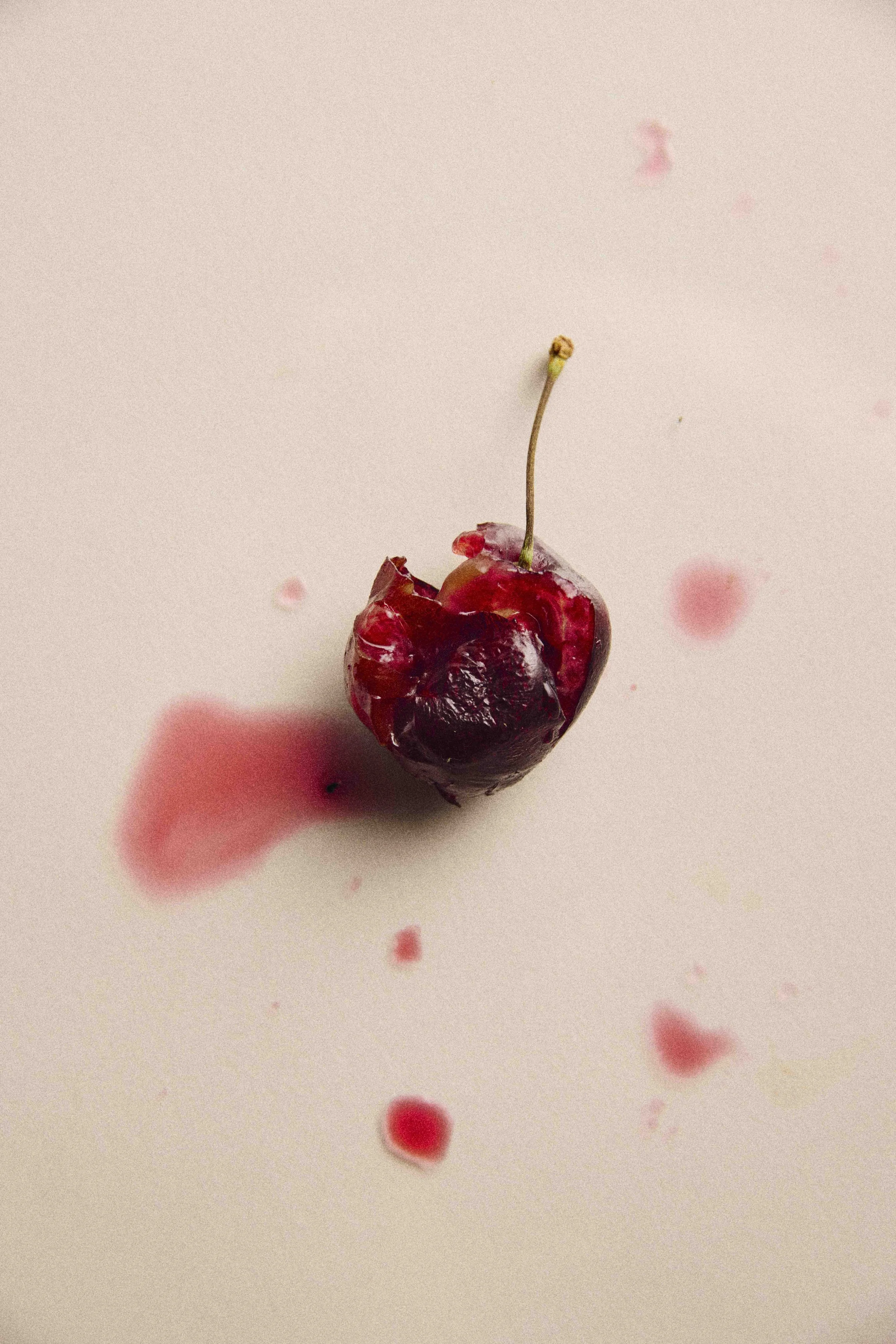Aufgebrochene rote Kirsche mit austretendem Saft und roten Flecken auf hellem Untergrund.