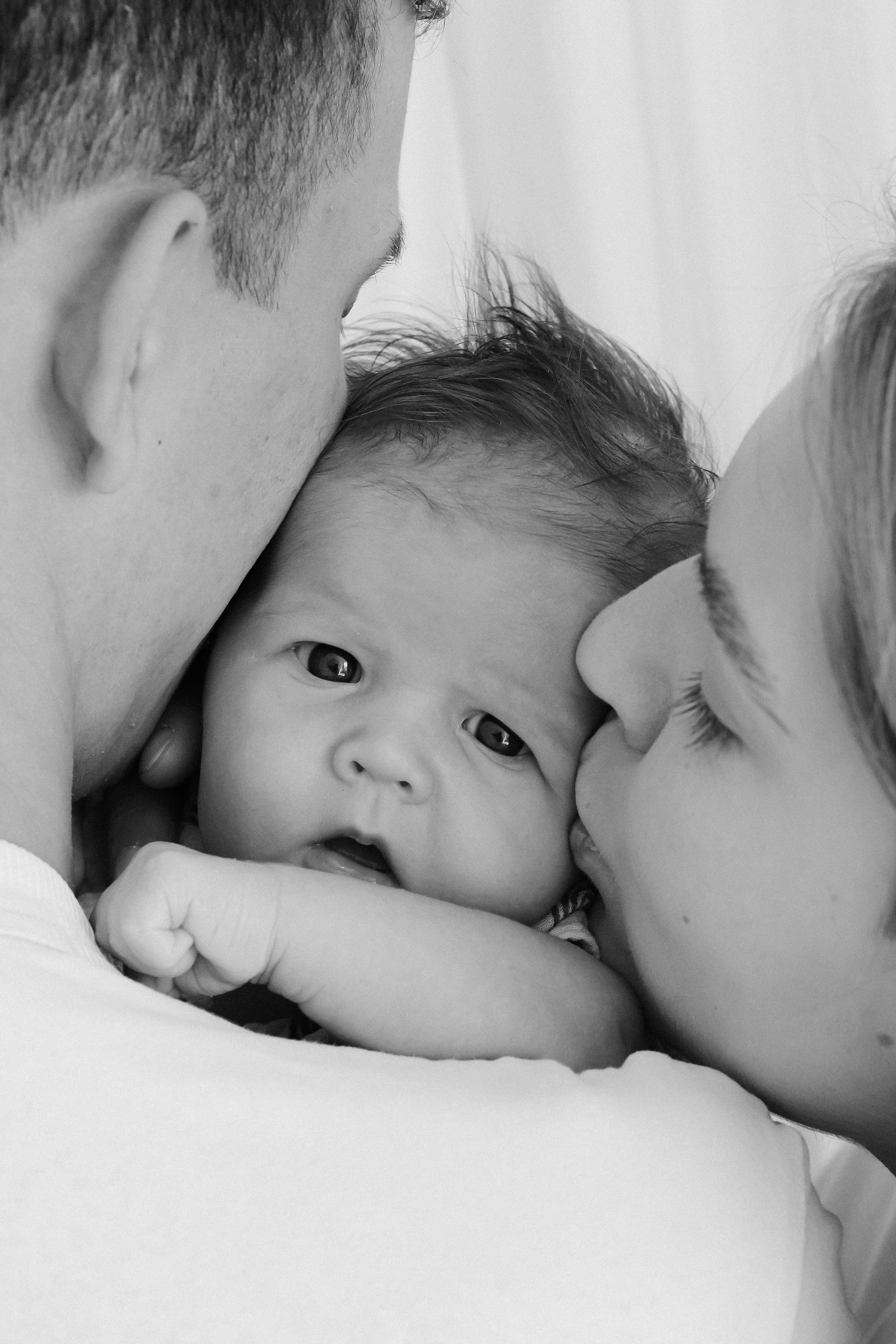 A mother and father each kissing a newborn baby on the check.