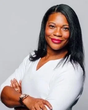 A woman with straight black hair, wearing a white top, smiling with arms crossed against a neutral background.