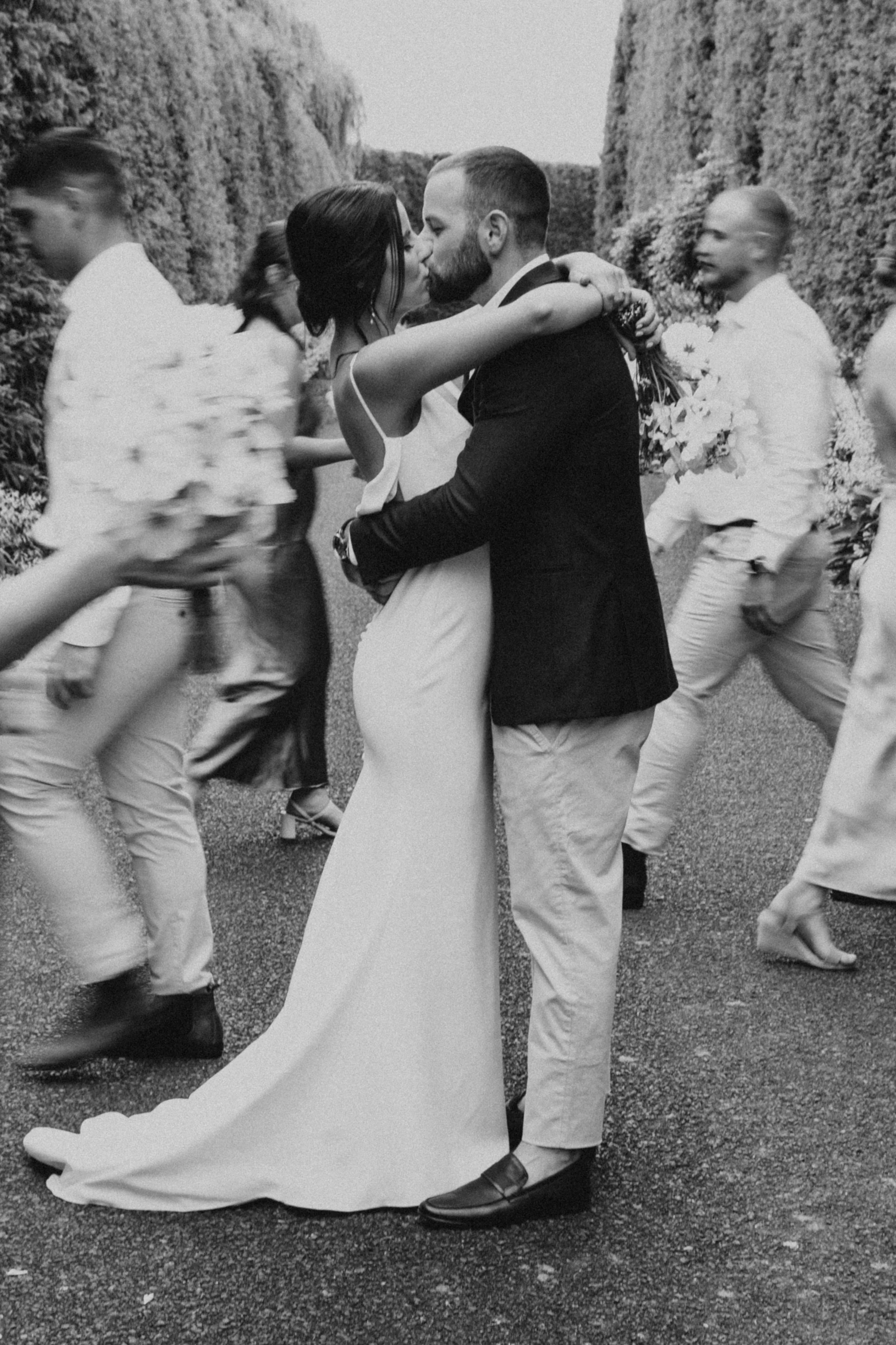 Waikato wedding Black and white photo of a couple kissing in wedding attire, surrounded by blurred motion of people walking at Hamilton wedding.