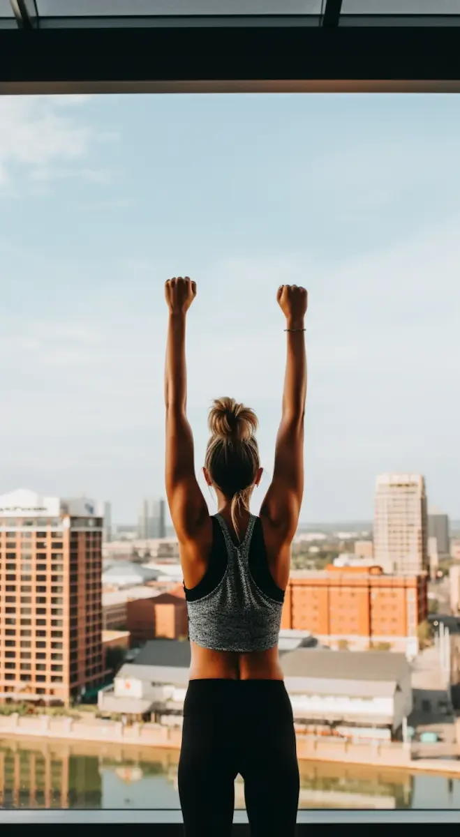 Woman triumphantly raising arms while overlooking cityscape.