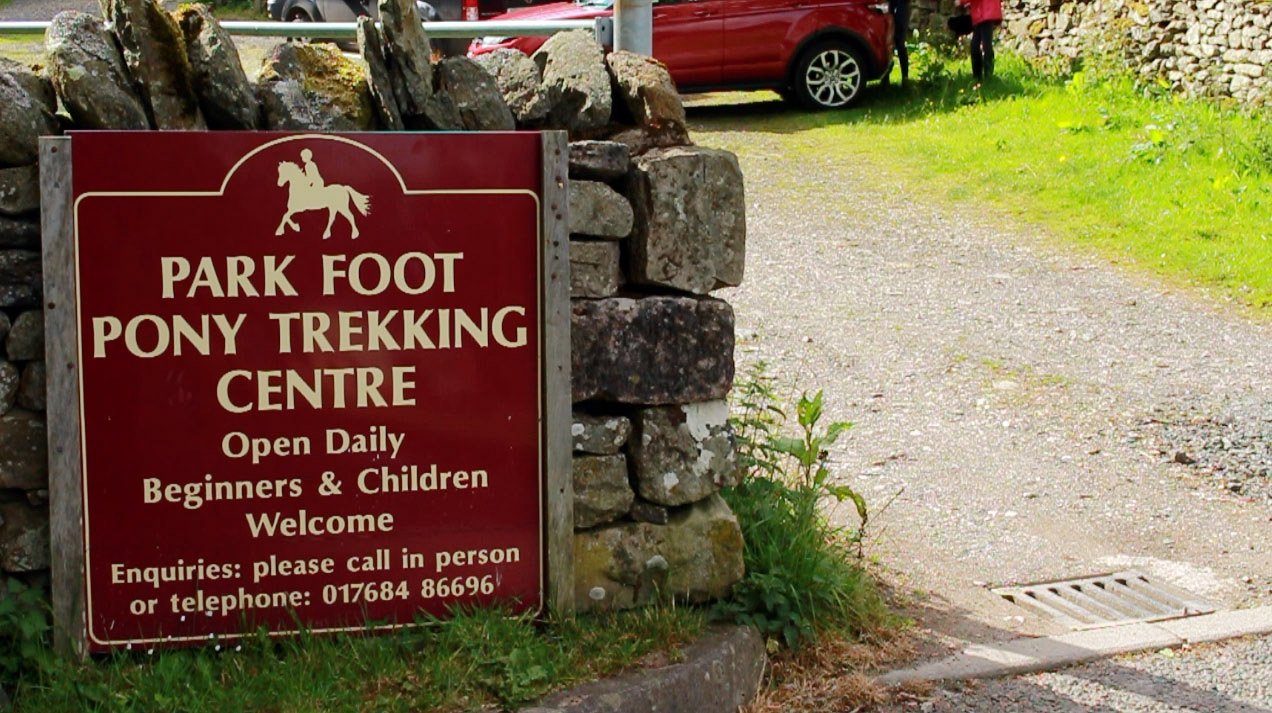 Sign for Park Foot Pony Trekking Centre with stony wall and red car nearby.