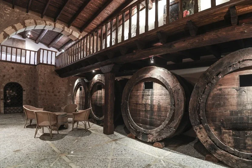 Large wine barrels stored inside a rustic cellar with a small seating area.