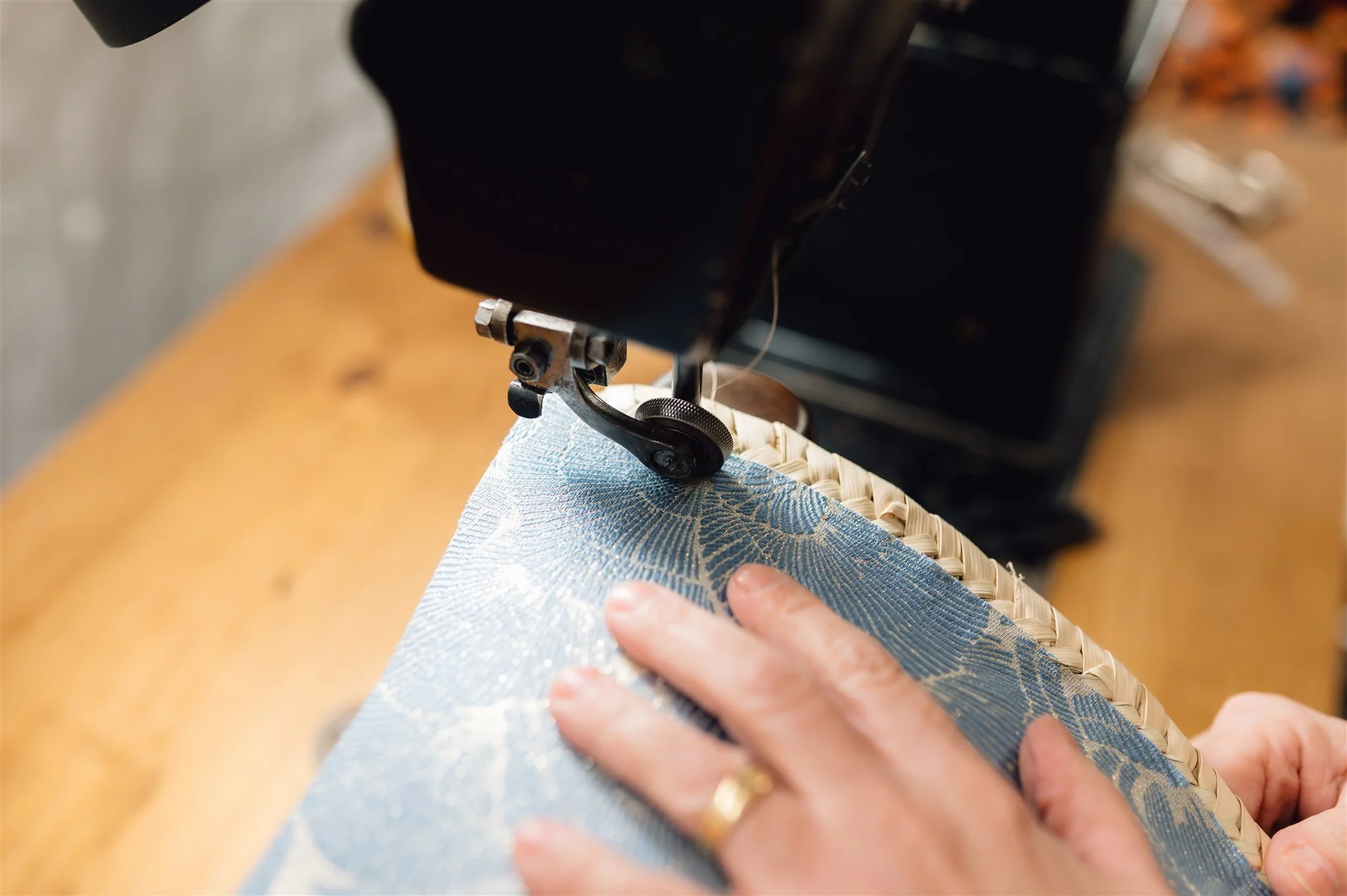 A person sewing a blue patterned fabric on a sewing machine.