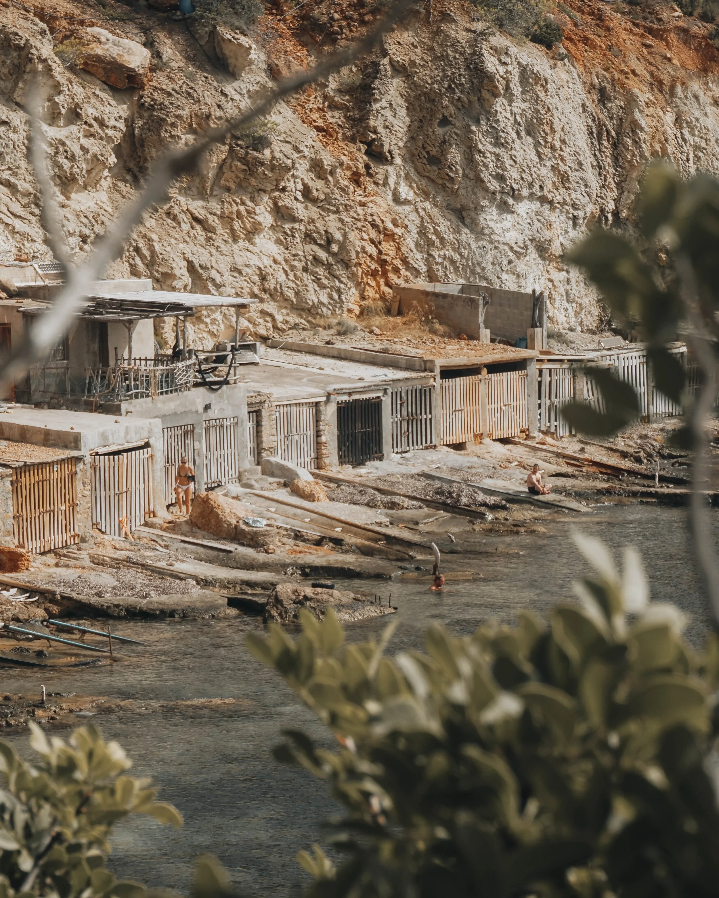 Rocky ibiza coastal area with small concrete structures and boat garages near the water.