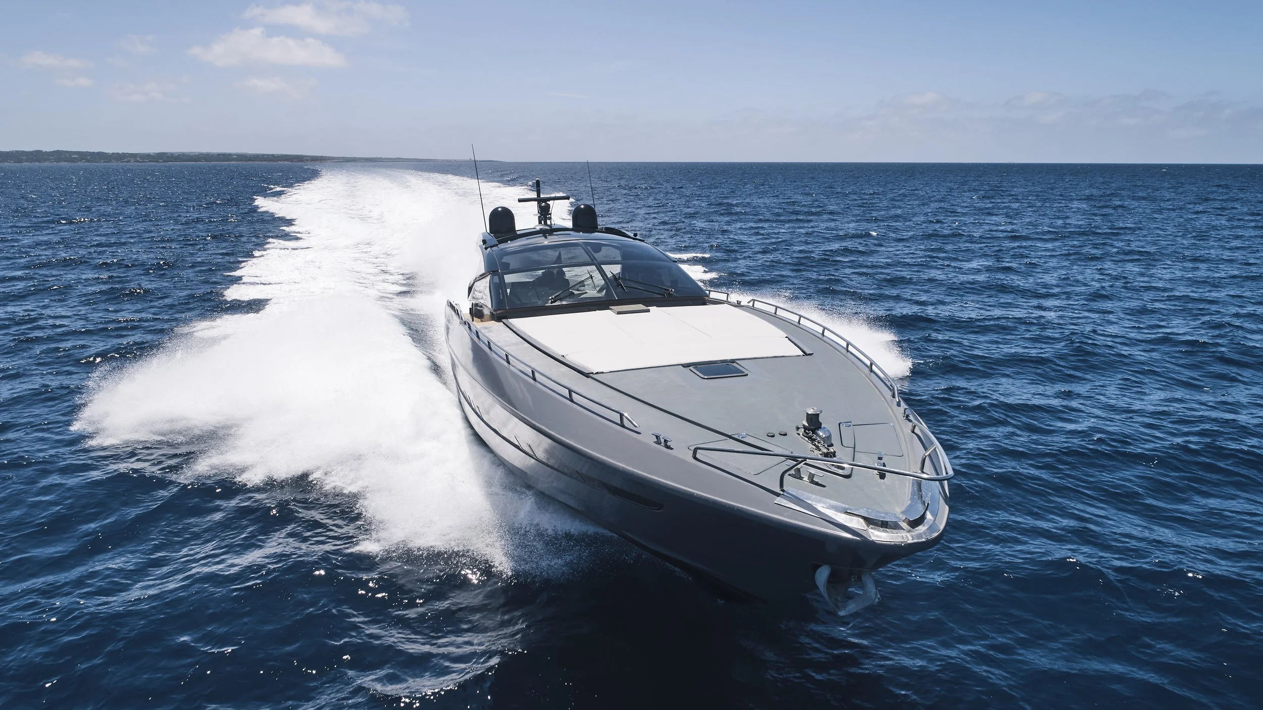 A luxury yacht speeding across the ocean, creating a large wake against a clear blue sky.