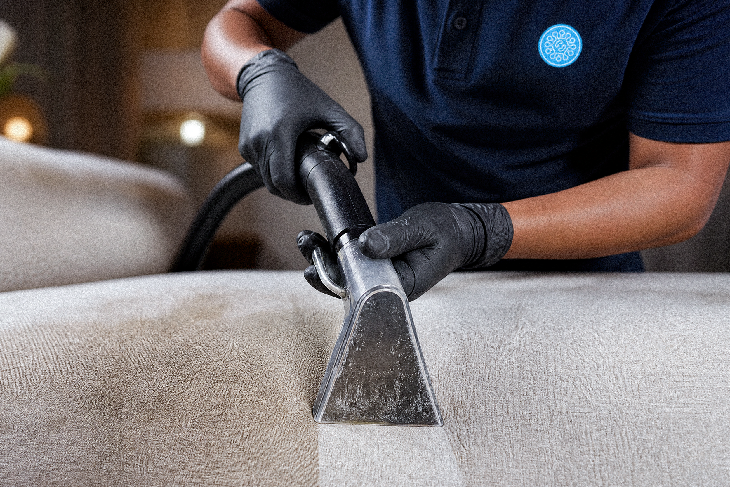 A person wearing black gloves and a dark blue shirt operating a carpet cleaning machine on a beige carpet.