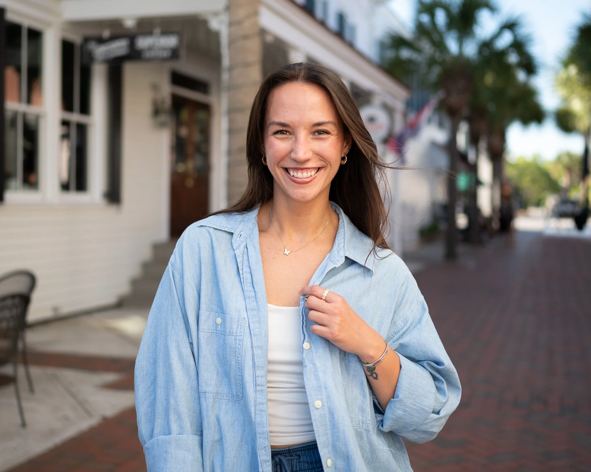 Woman in a denim jacket leaning against a storefront on a charming downtown street, smiling confidently for a headshot photoshoot.