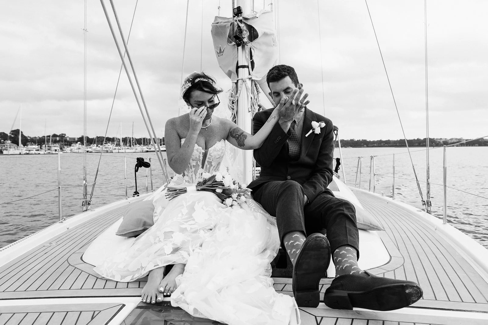 Black‑and‑white photo of a couple toasting on a sailboat deck, laughing and clinking glasses.