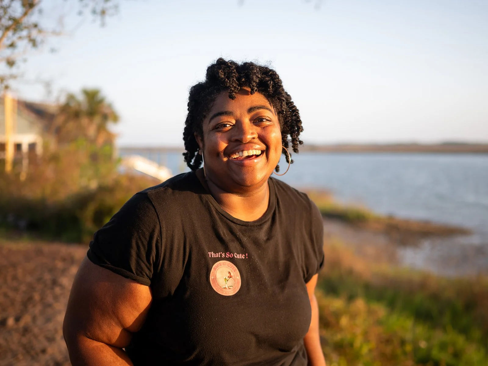 Woman with curly hair standing near the water at sunset, eyes closed and serene expression for Lowcountry headshot photoshoot