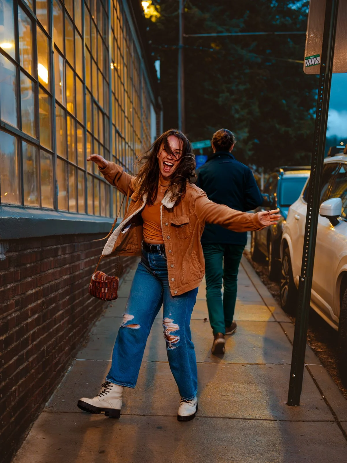 Woman dancing joyfully in front of an urban building at night, city lights glowing behind her.