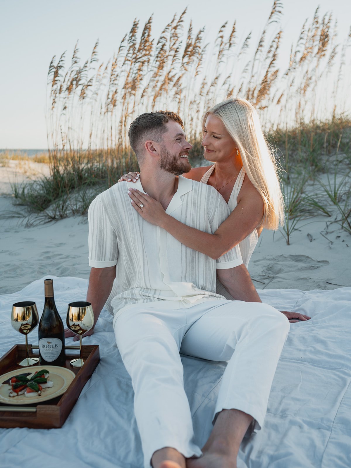 Couple sitting on the beach wrapped in a blanket, watching the sunset together.