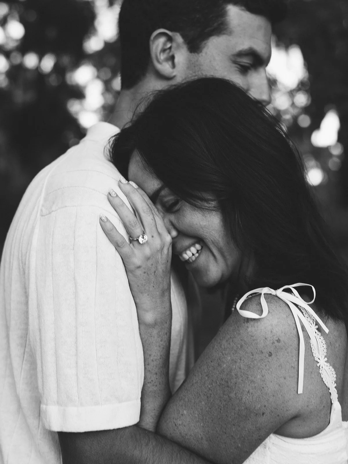 Black‑and‑white photo of a couple sharing an intimate hug in a field, eyes closed.