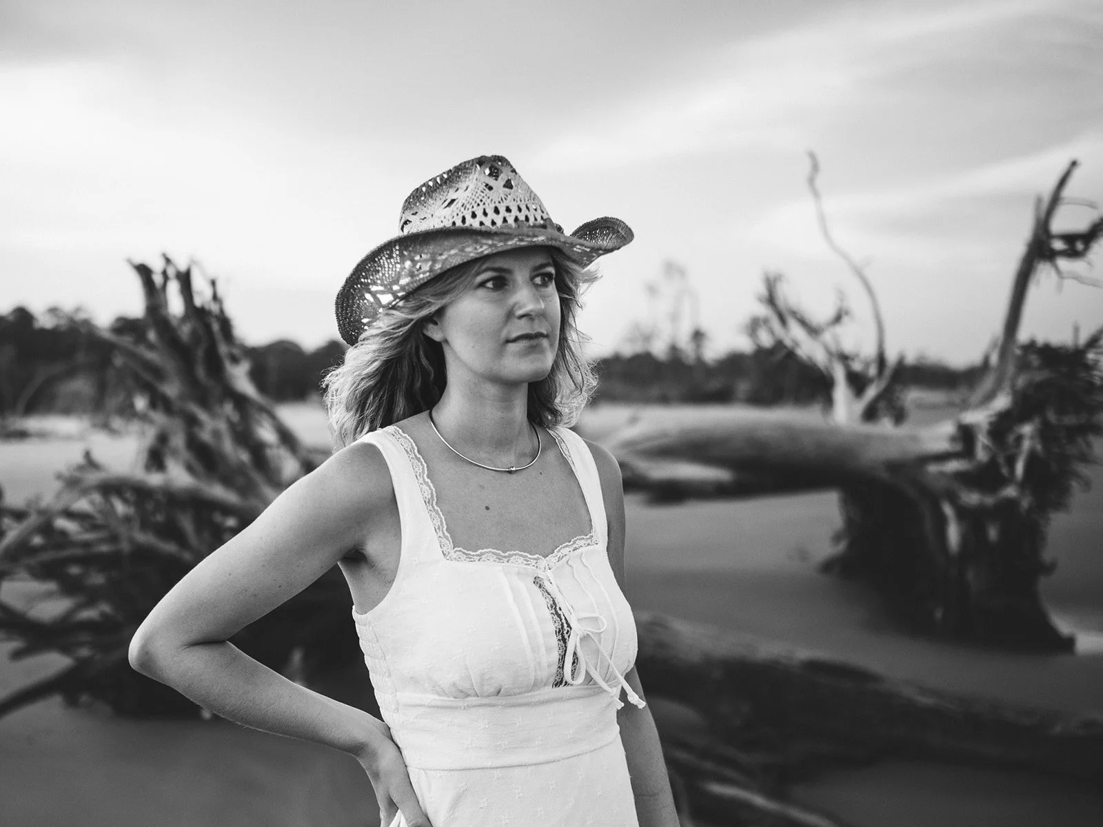 Woman with a straw hat walking on driftwood beach, long hair blowing in the wind.