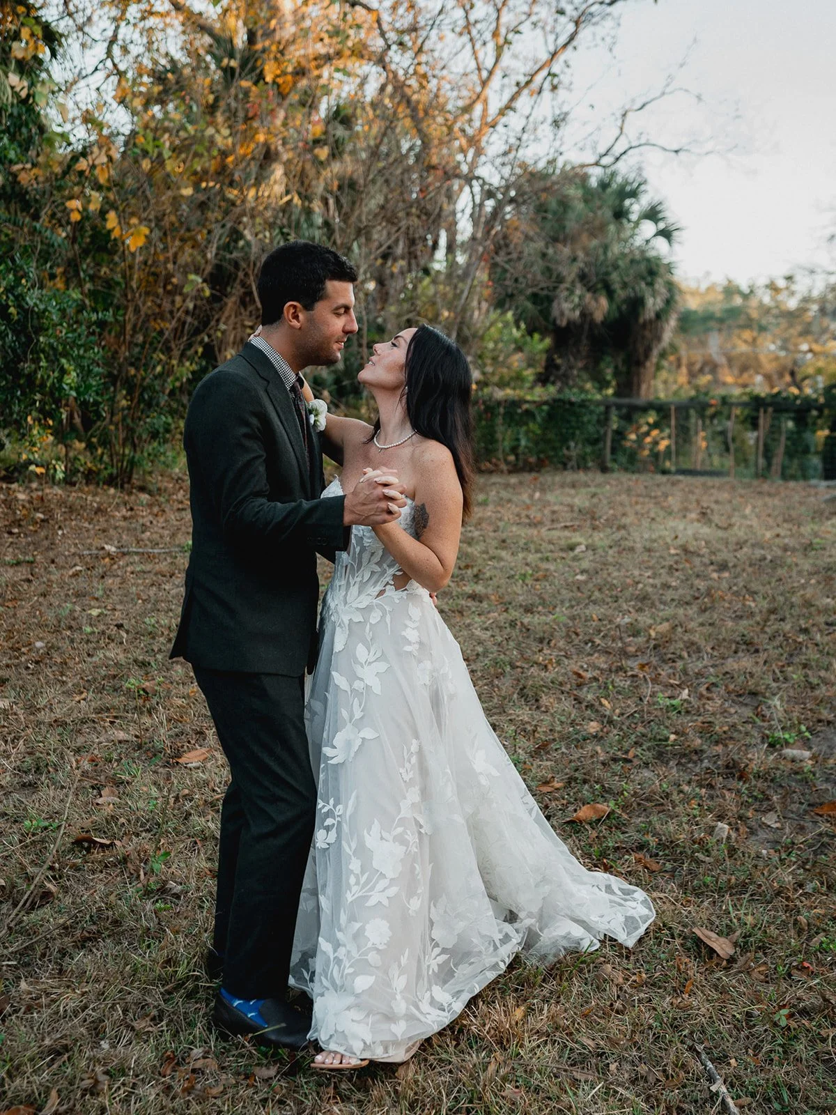 Newlyweds dancing together in a field surrounded by garden greenery and soft sunlight.