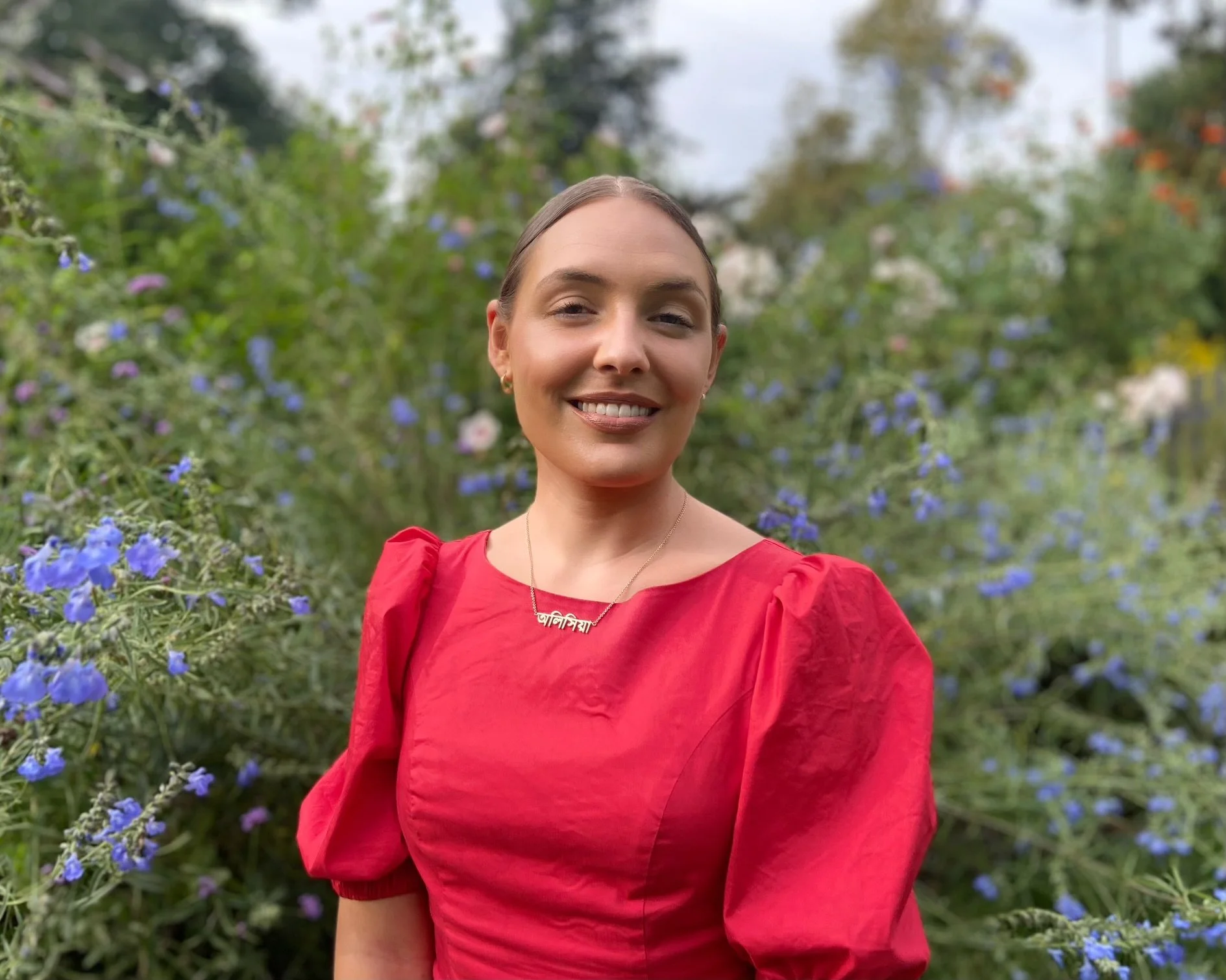 Alicia Chatterjee, Ph.D, LSW wears a red dress and sits in a meadow with flowers