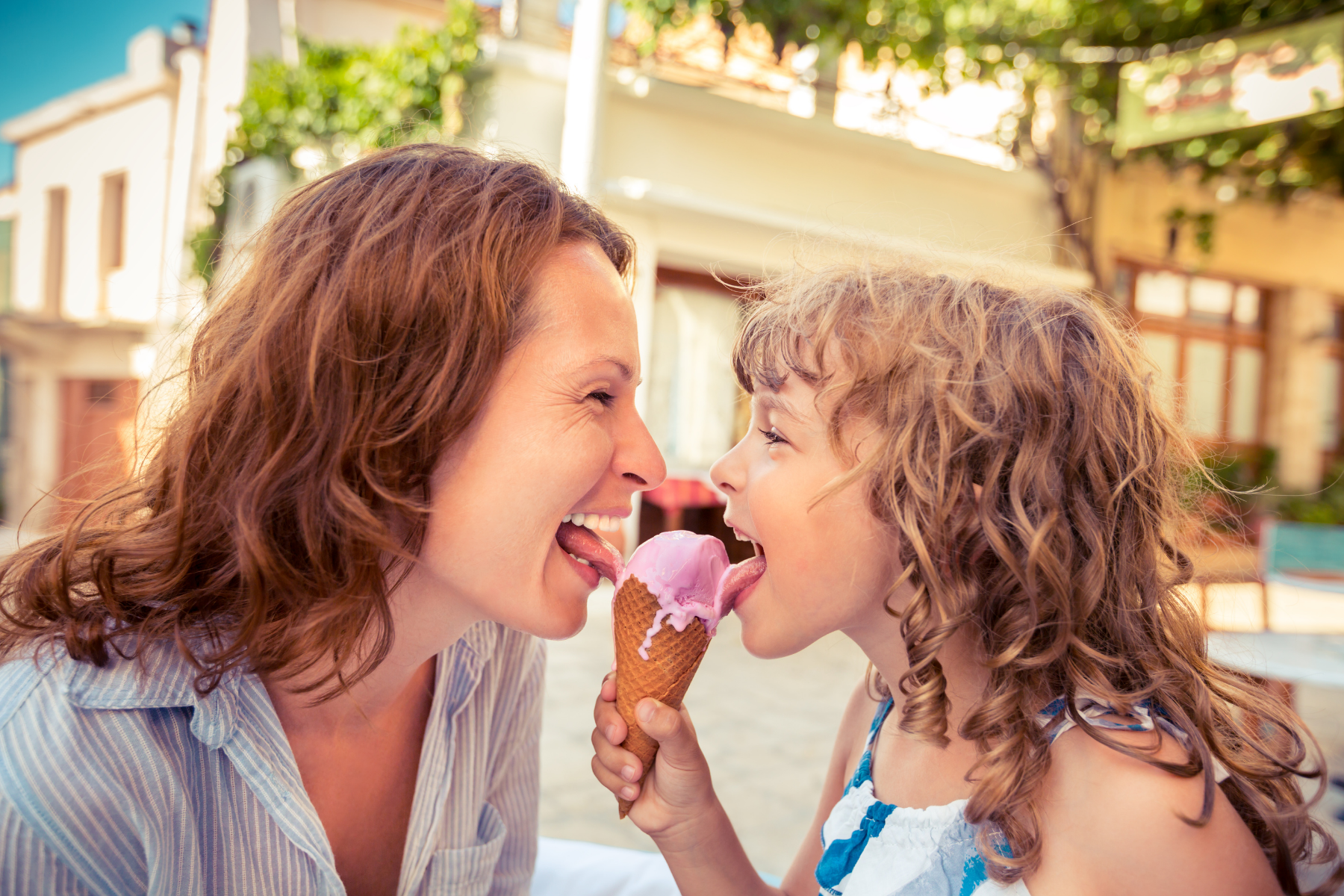Mother and daugher sharing a scoop of strawberry ice cream on a waffle cone