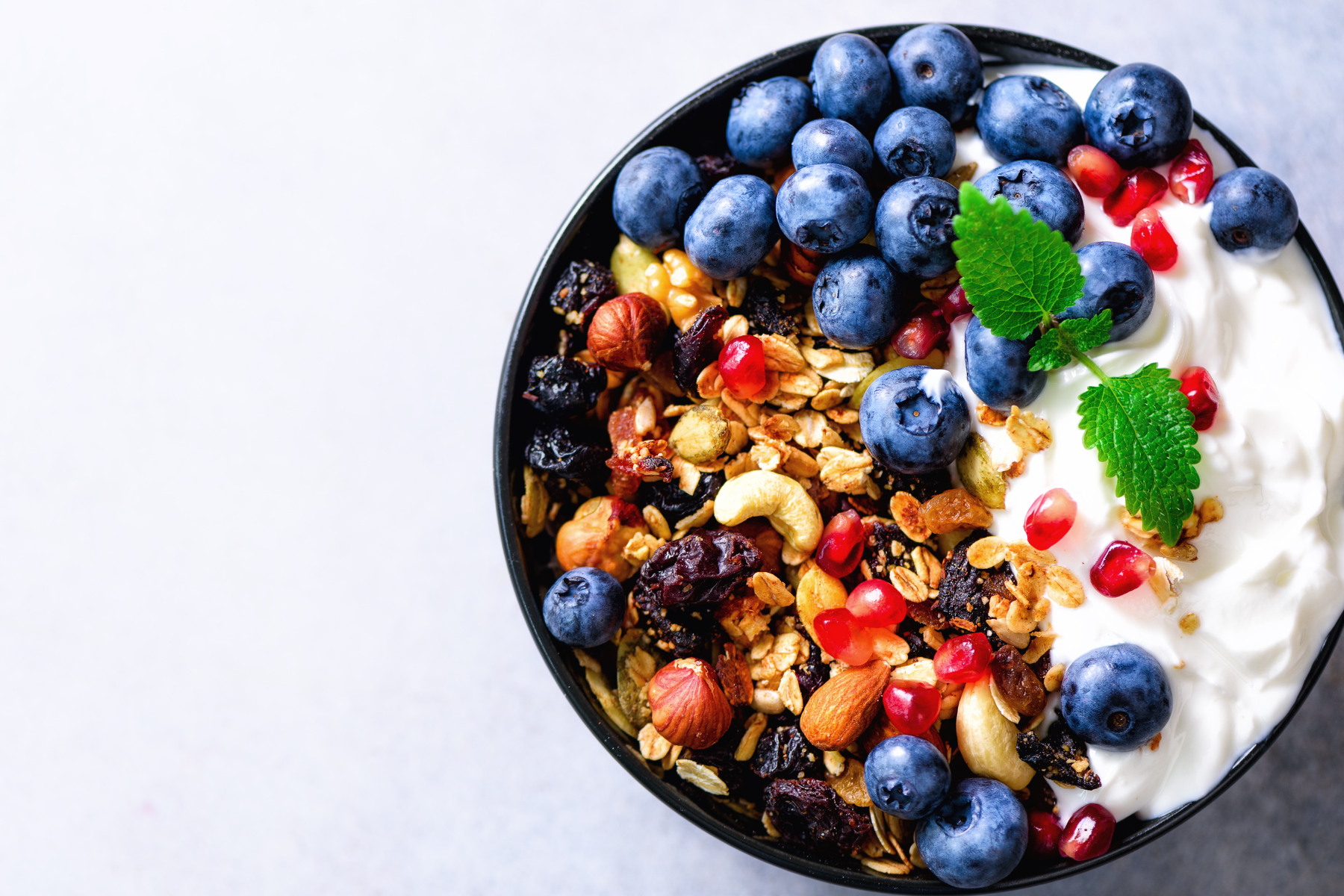 bowl of greek yogurty with fresh blueberries, pomegranate seeds, granola, and nuts