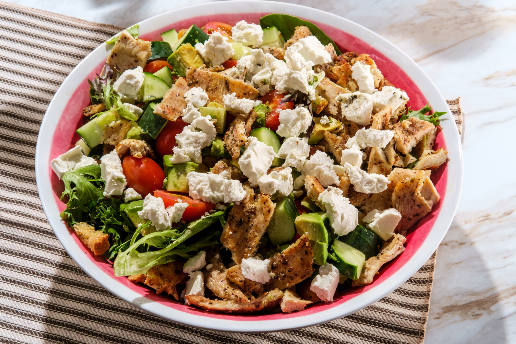 grilled chicken salad with tomato, cucumber, avocado and feta cheese on a bed of mixed greens